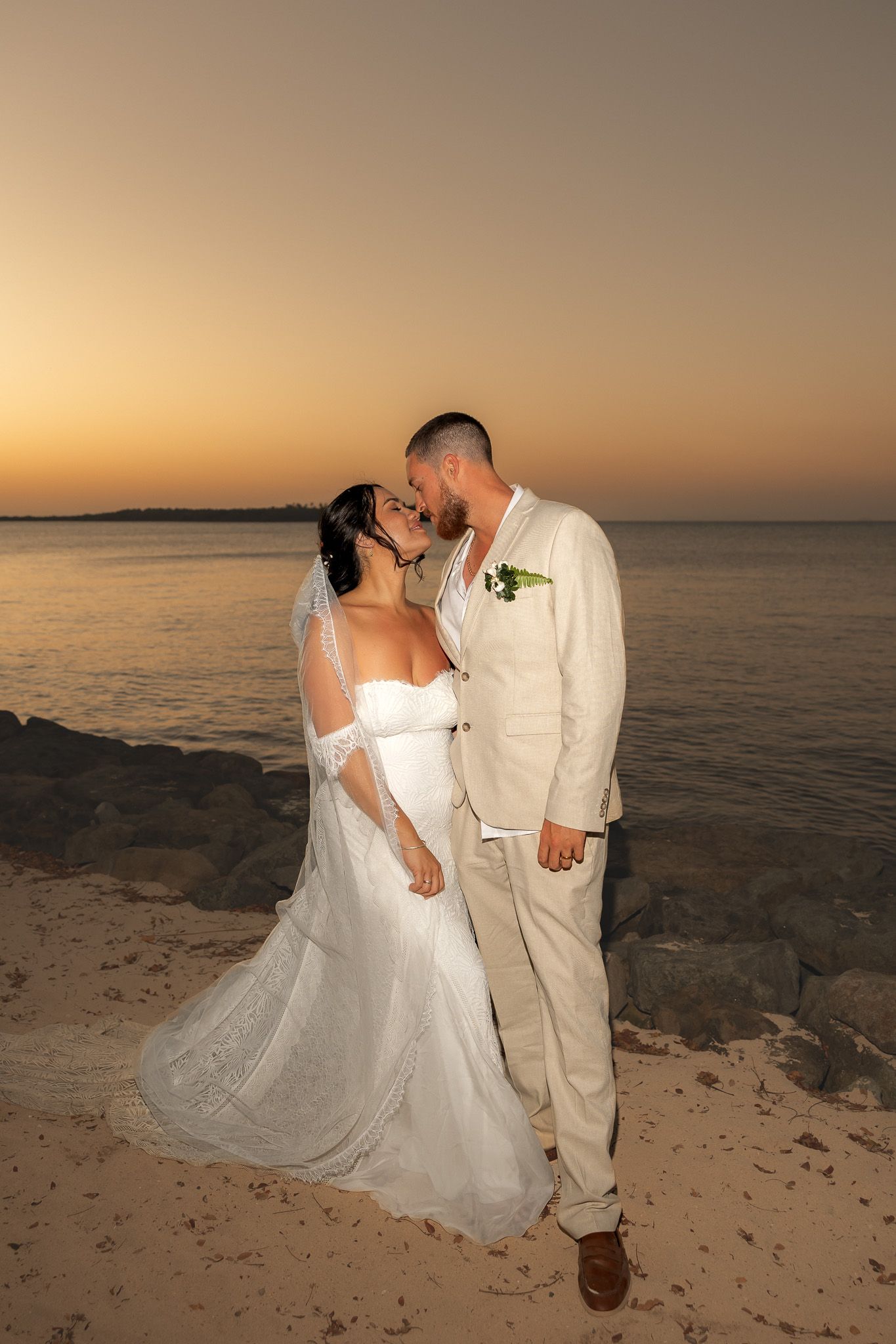 Bride and groom share a romantic kiss on the beach at golden sunset during their wedding.
