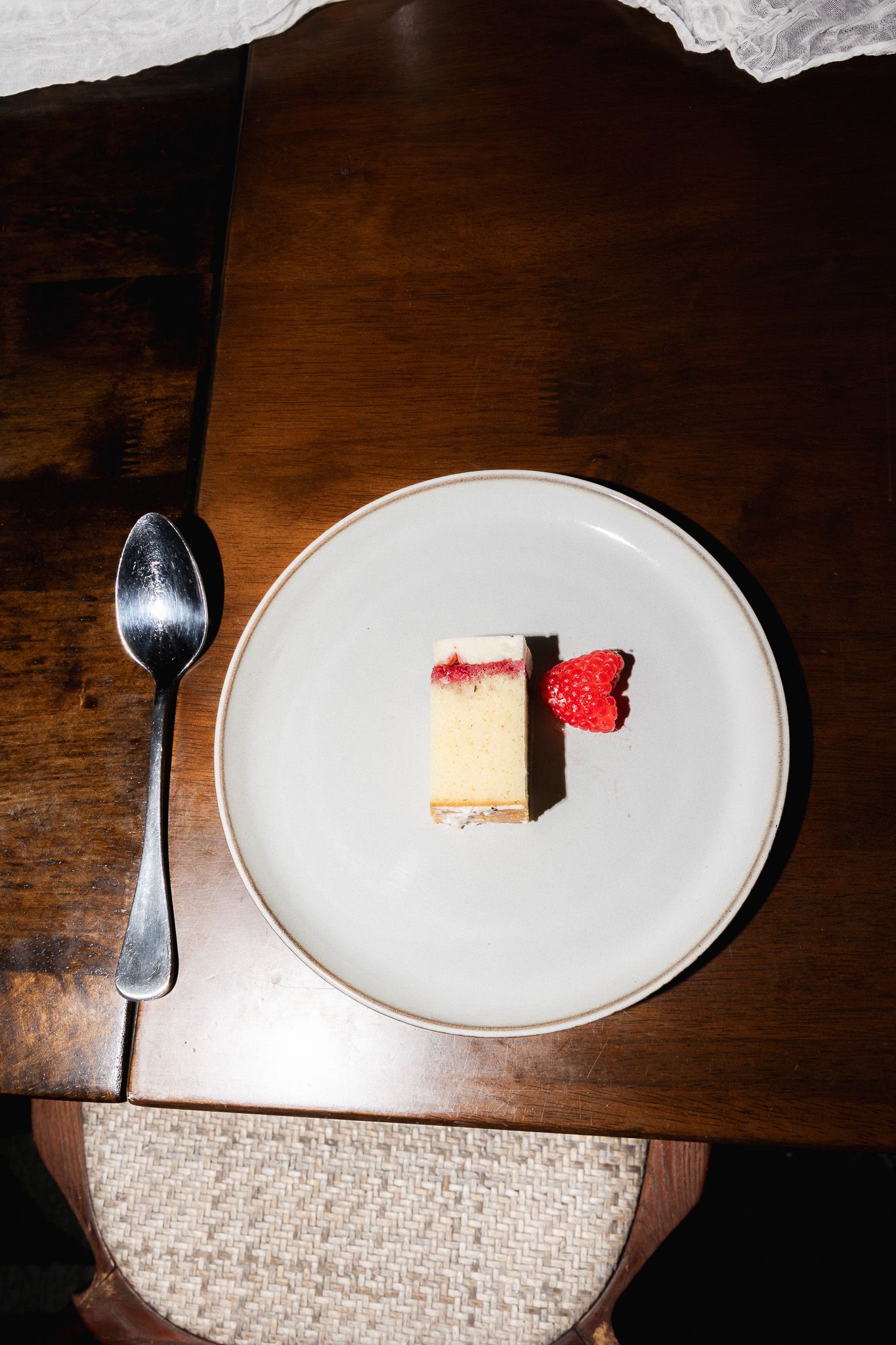 Overhead view of a slice of strawberry cheesecake on white plate with silver spoon on wooden table.