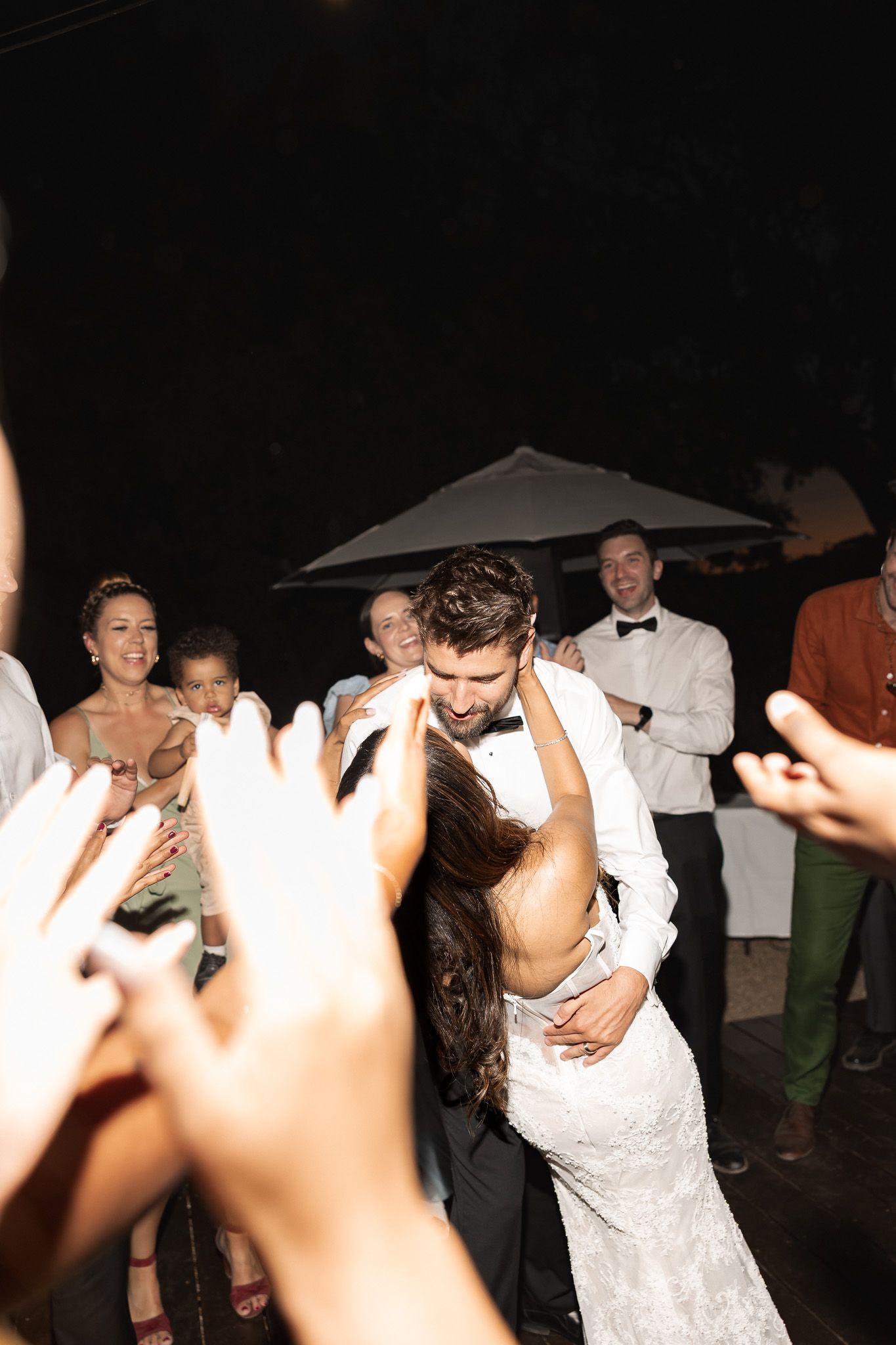 Bride and groom share romantic first dance dip surrounded by cheering guests at night reception.