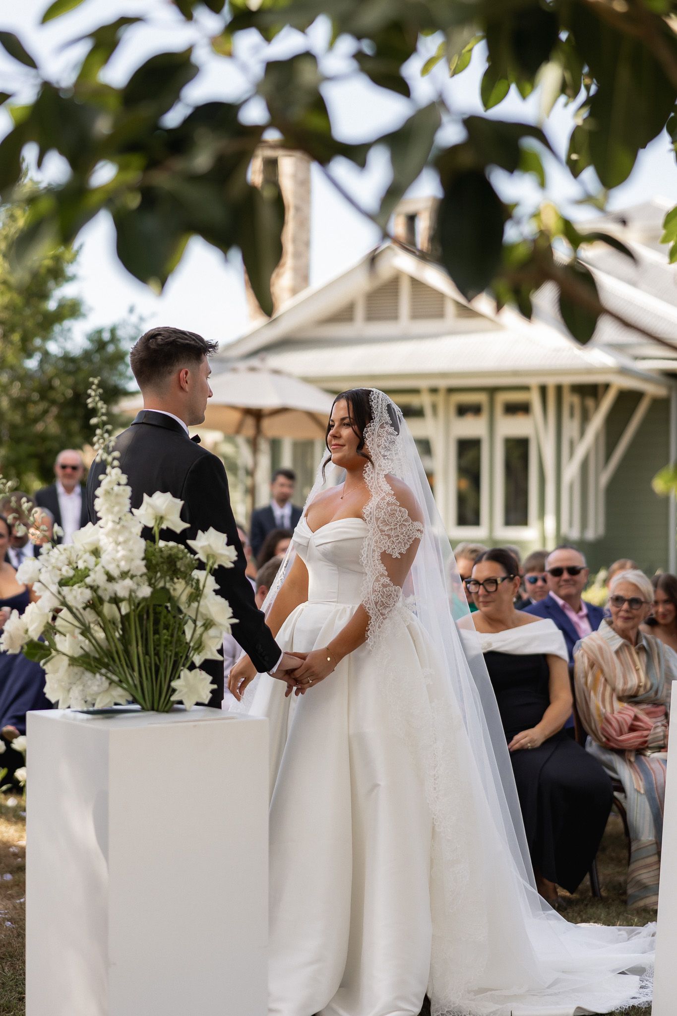 Bride and groom exchange vows outdoors at elegant garden wedding ceremony with white floral arrangements.