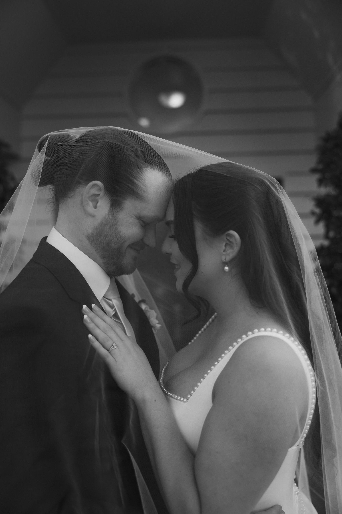 Black and white wedding photo of bride and groom sharing intimate moment under veil outside church.