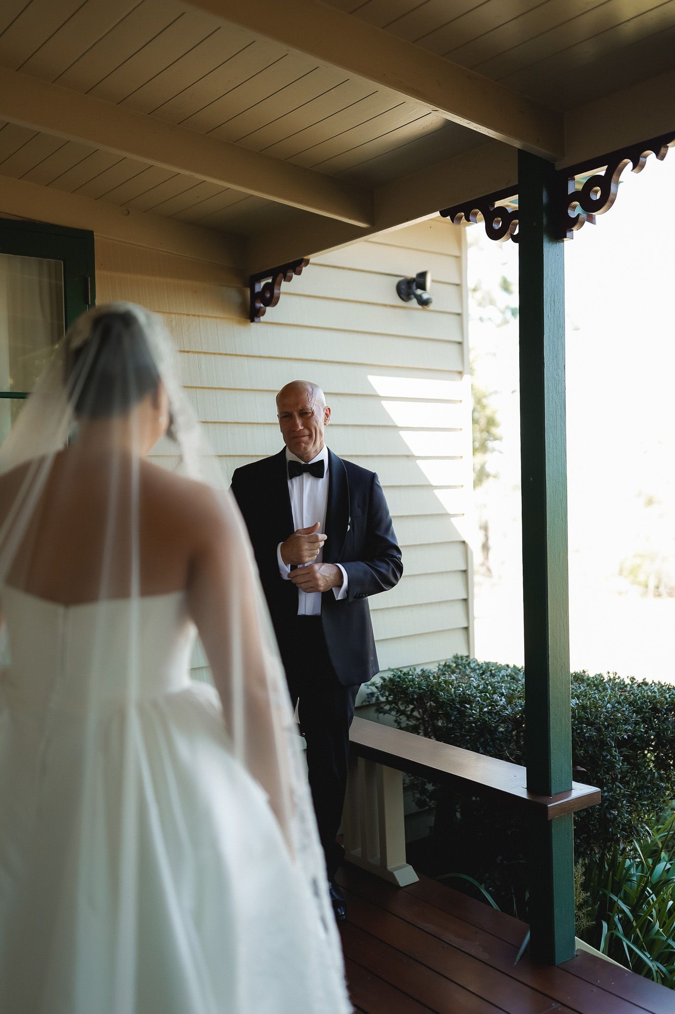 Emotional father-daughter first look moment on porch, bride in white gown and veil facing man in navy tuxedo.