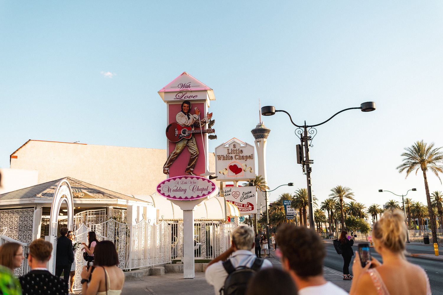 Tourists gather near the iconic Elvis-themed Little White Wedding Chapel sign on the Las Vegas Strip at dusk.