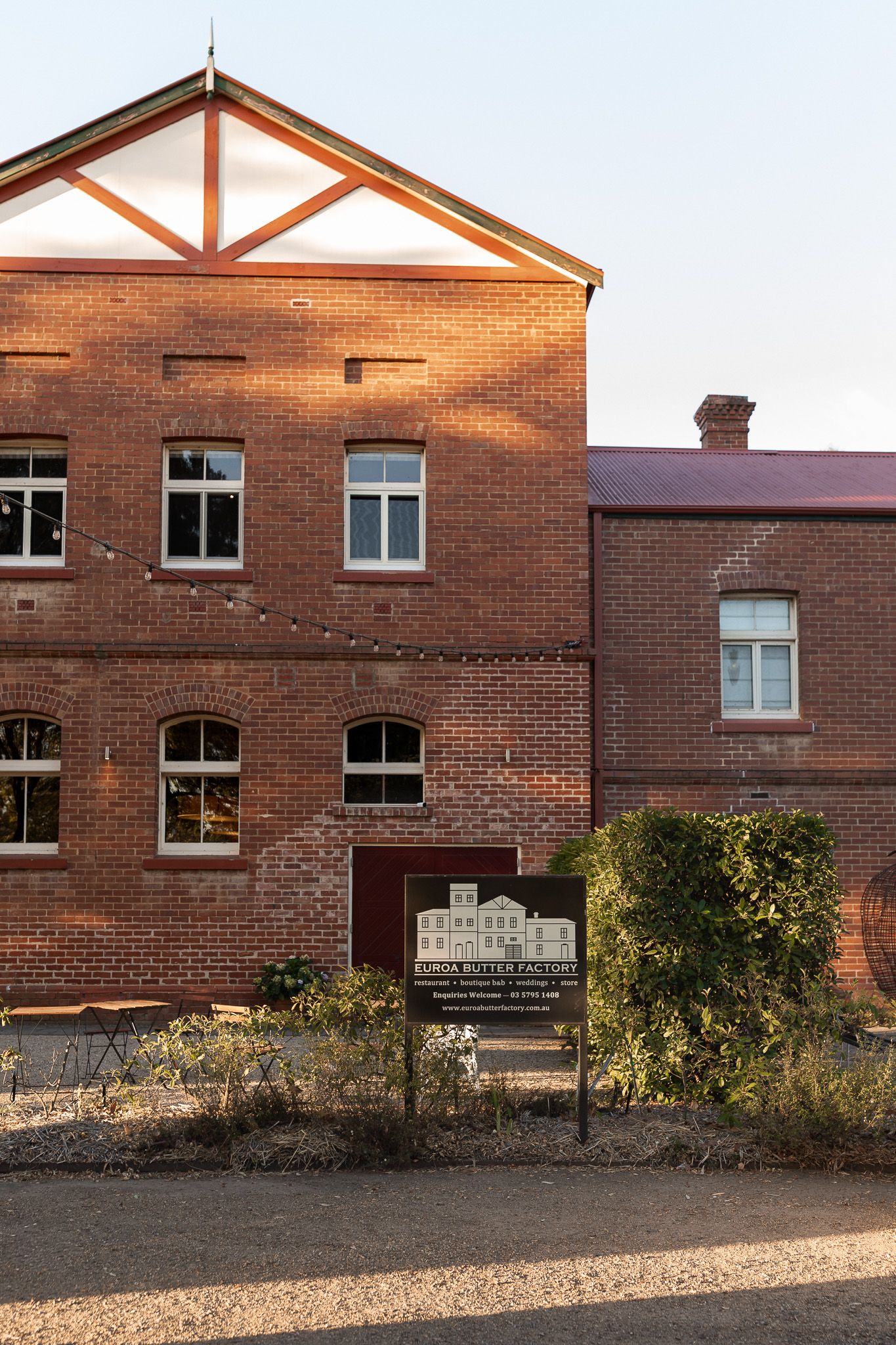 Historic red brick Euroa Butter Factory wedding venue with sign and string lights at sunset.