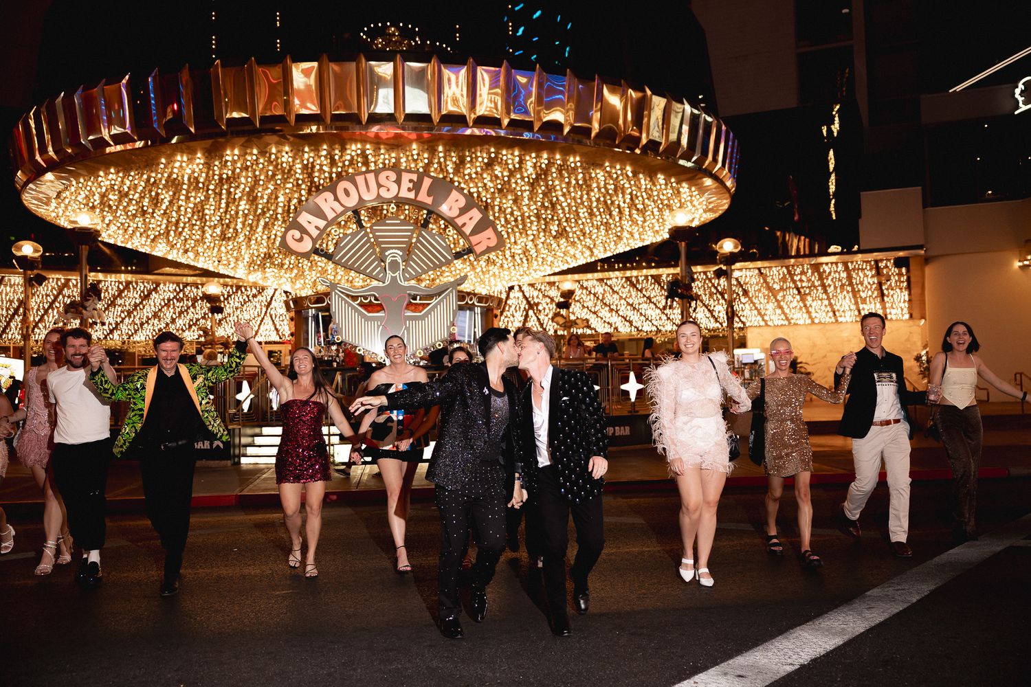 Wedding party celebrates under sparkling carousel lights on the Las Vegas Strip at night.