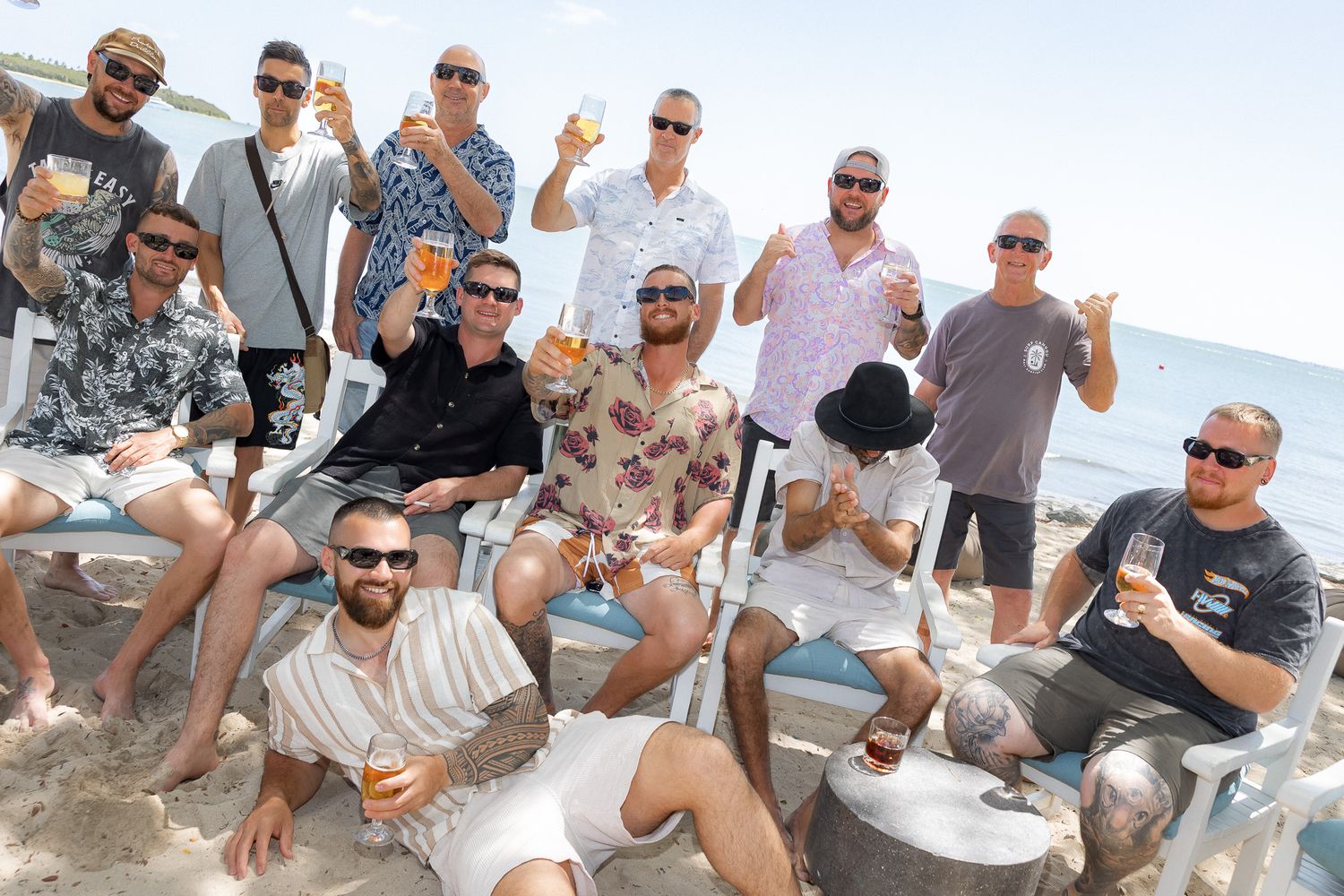 Group of men celebrating on a sunny beach, holding drinks and posing together for a photo at a seaside resort.