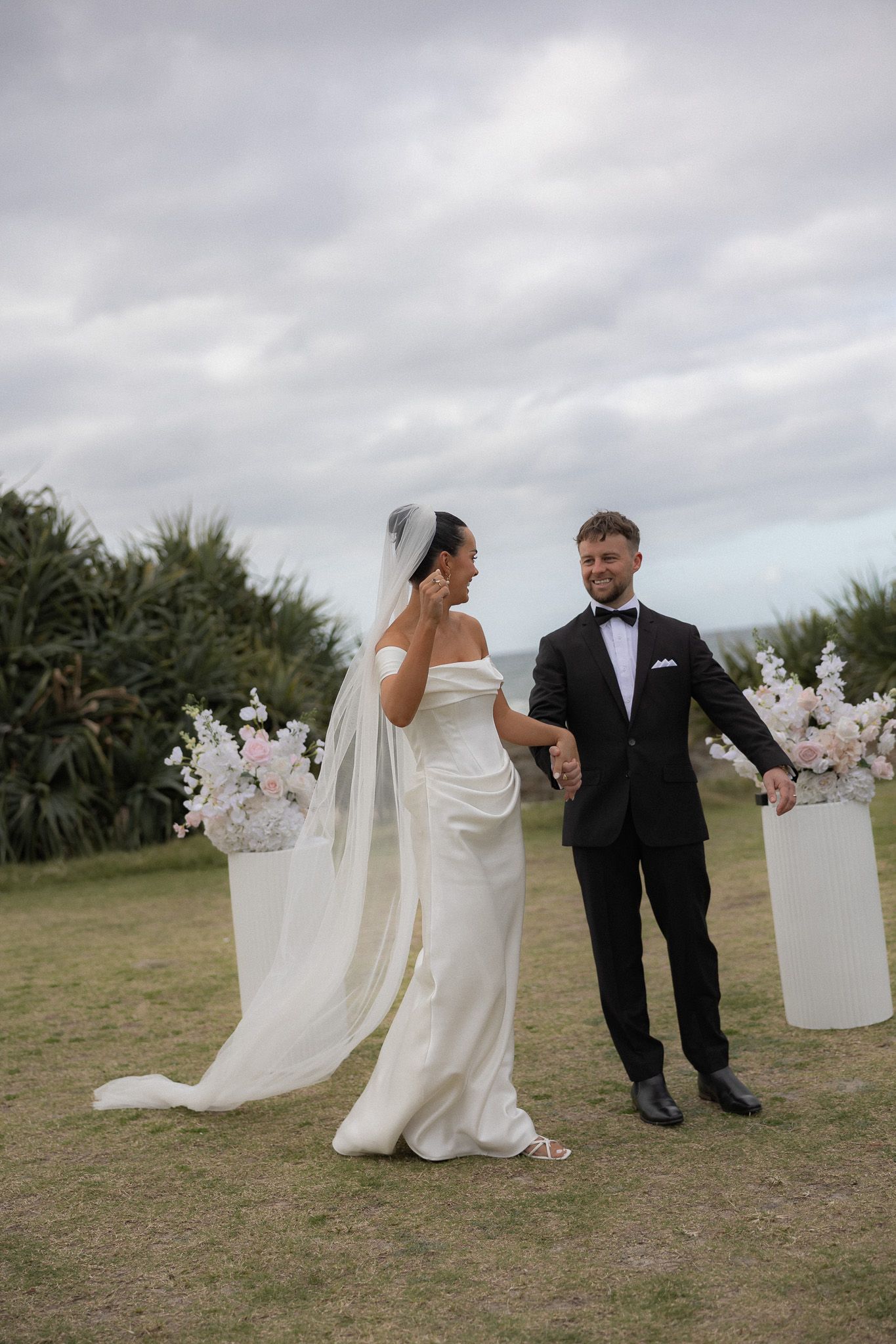 Bride and groom hold hands at outdoor ceremony with floral arrangements.