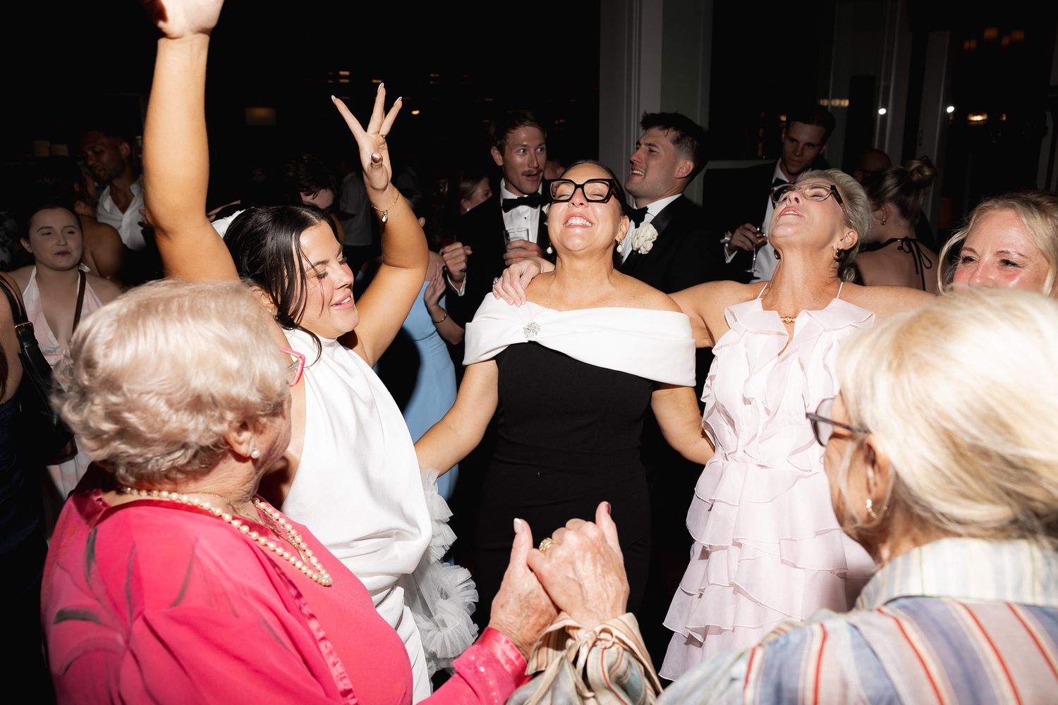 A joyful wedding guest in a black dress is lifted by friends on the dance floor during the reception.