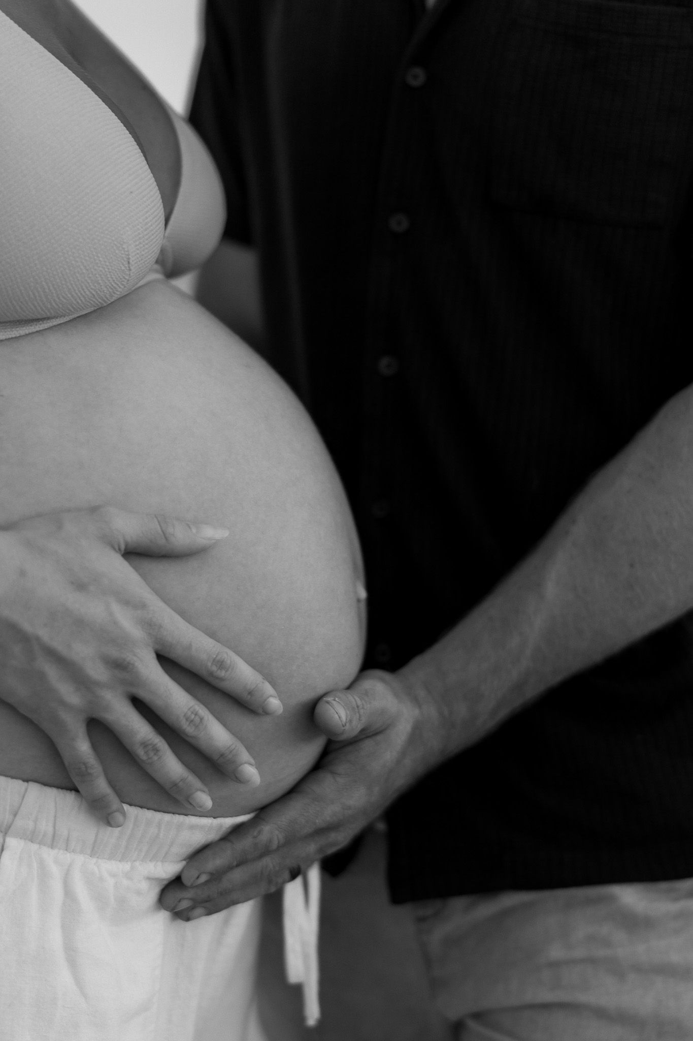 Black and white photo of a pregnant woman and partner cradling her baby bump together.