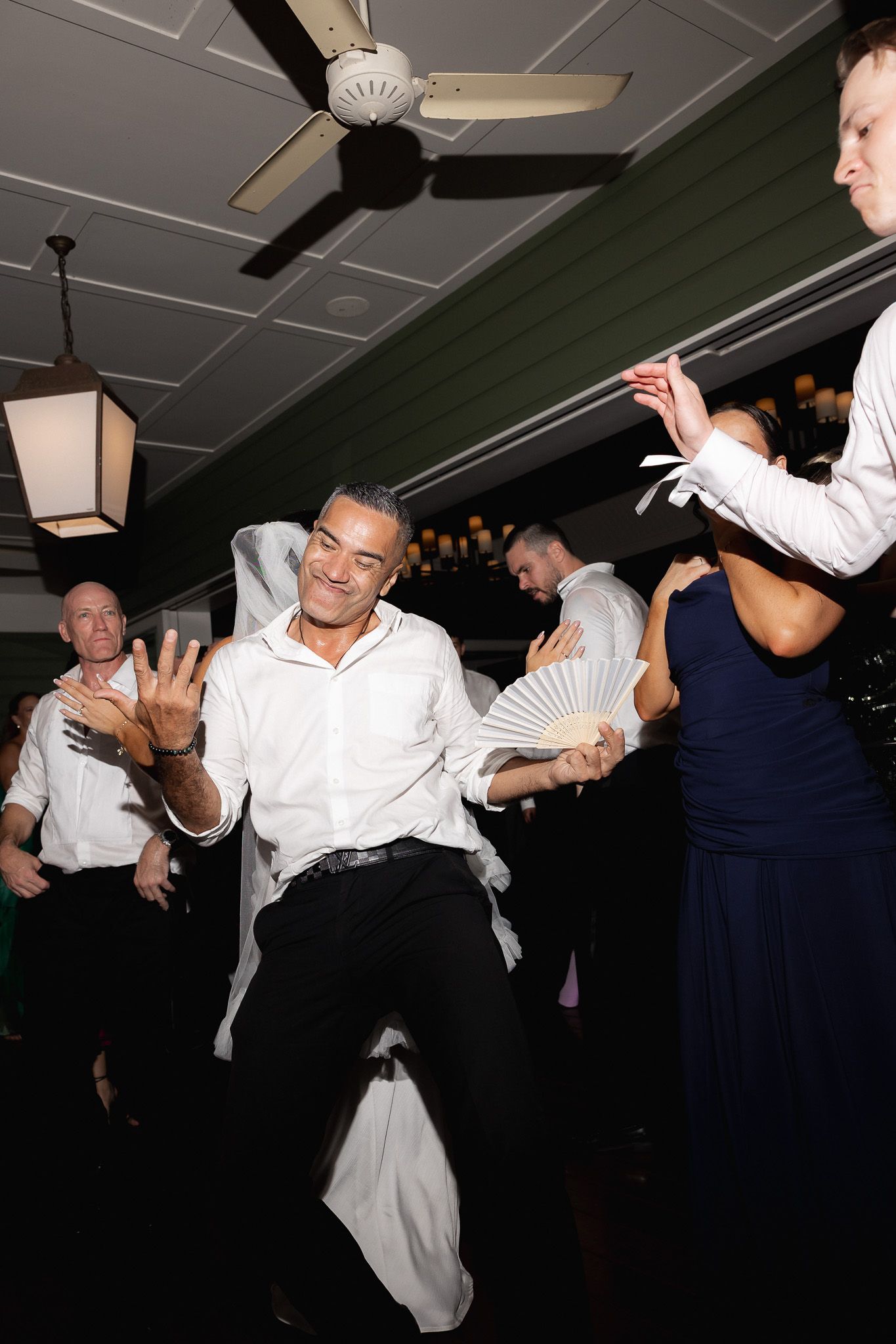 A wedding guest dances energetically on the dance floor while others celebrate around him at the reception.
