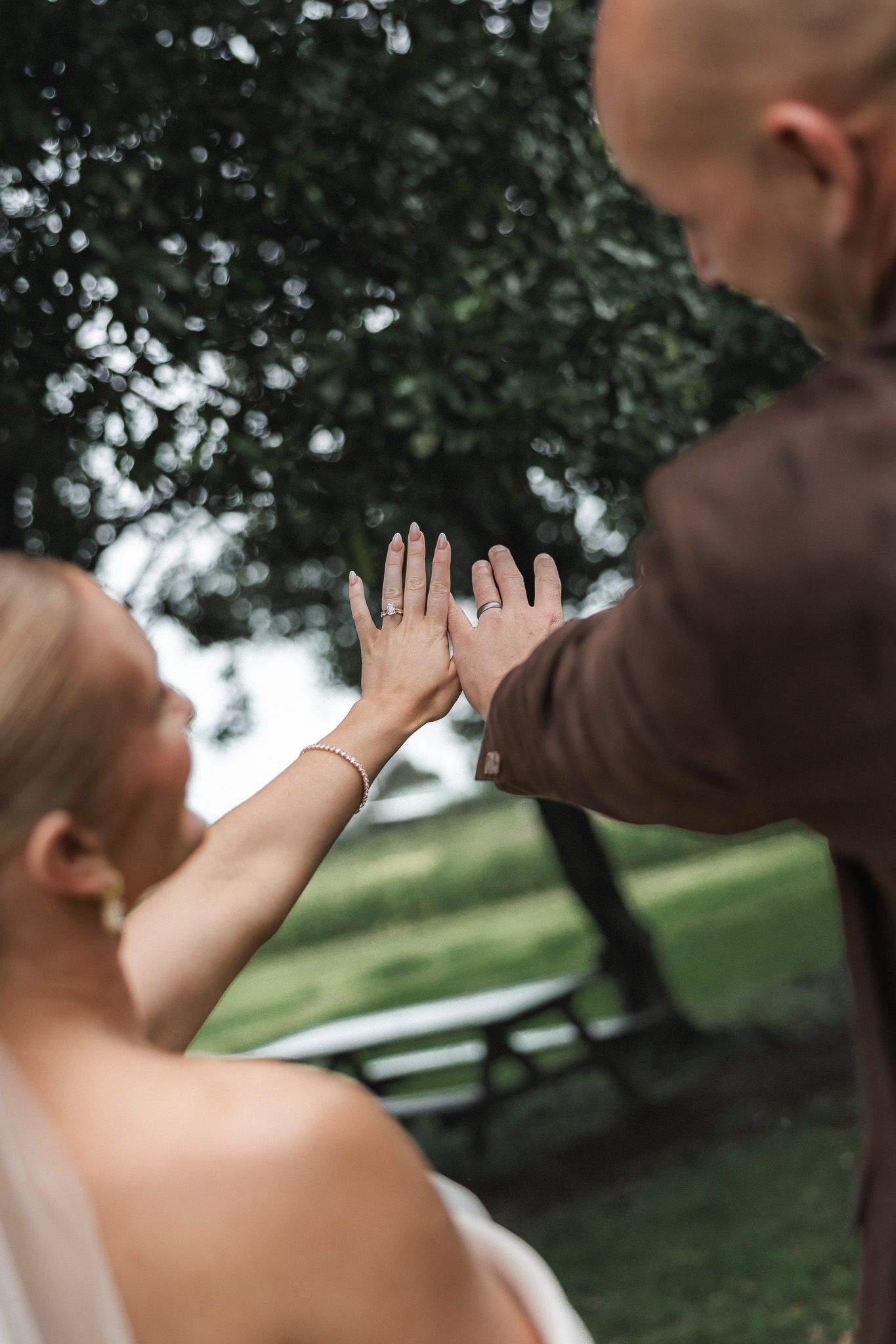Bride and groom pressing palms together showing wedding rings in outdoor park ceremony.