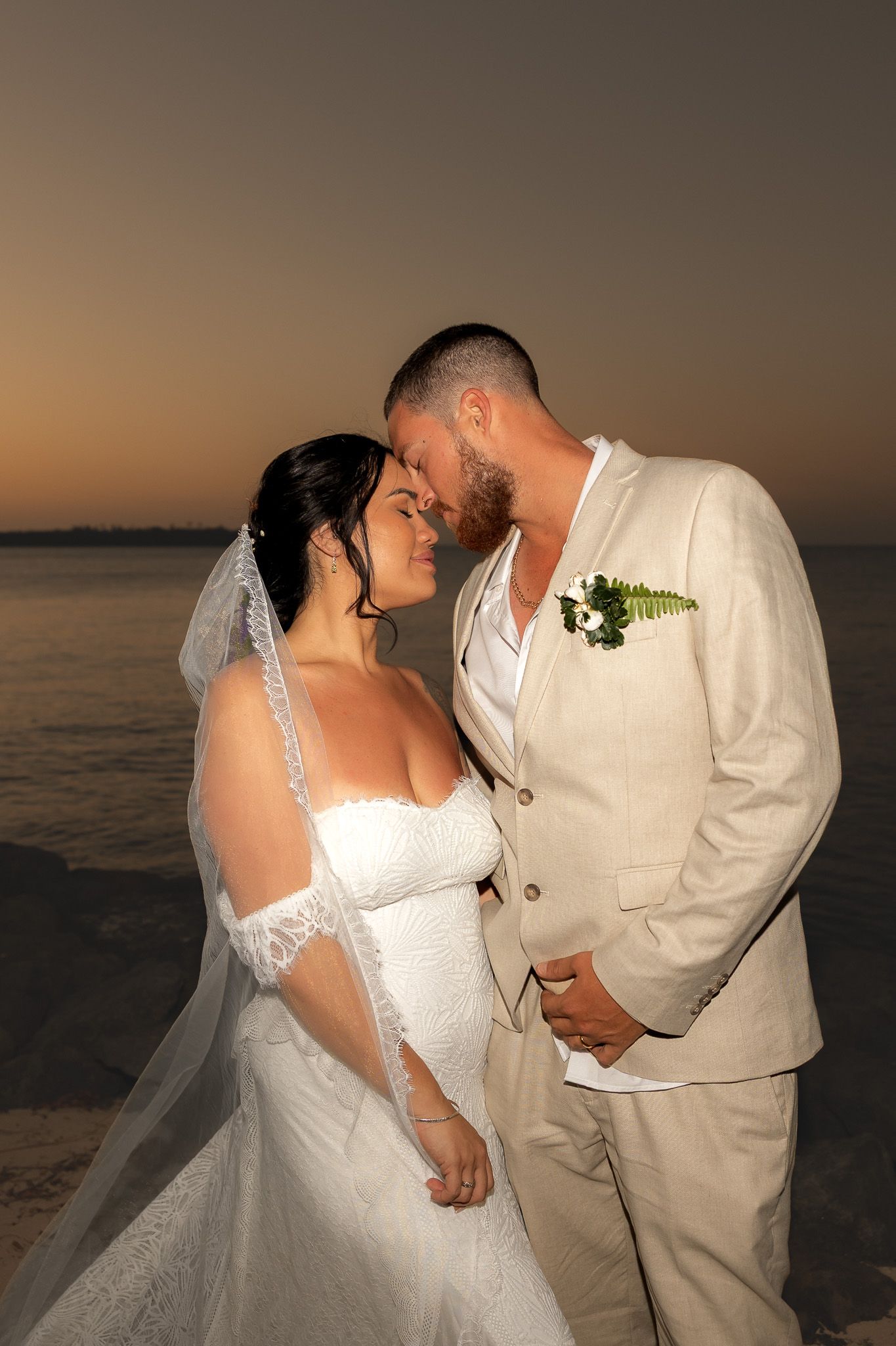 Bride and groom share a romantic sunset moment on the beach in wedding attire.