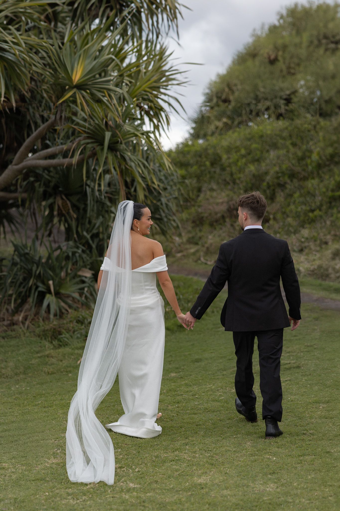 Bride and groom walk hand in hand through lush green garden after ceremony.