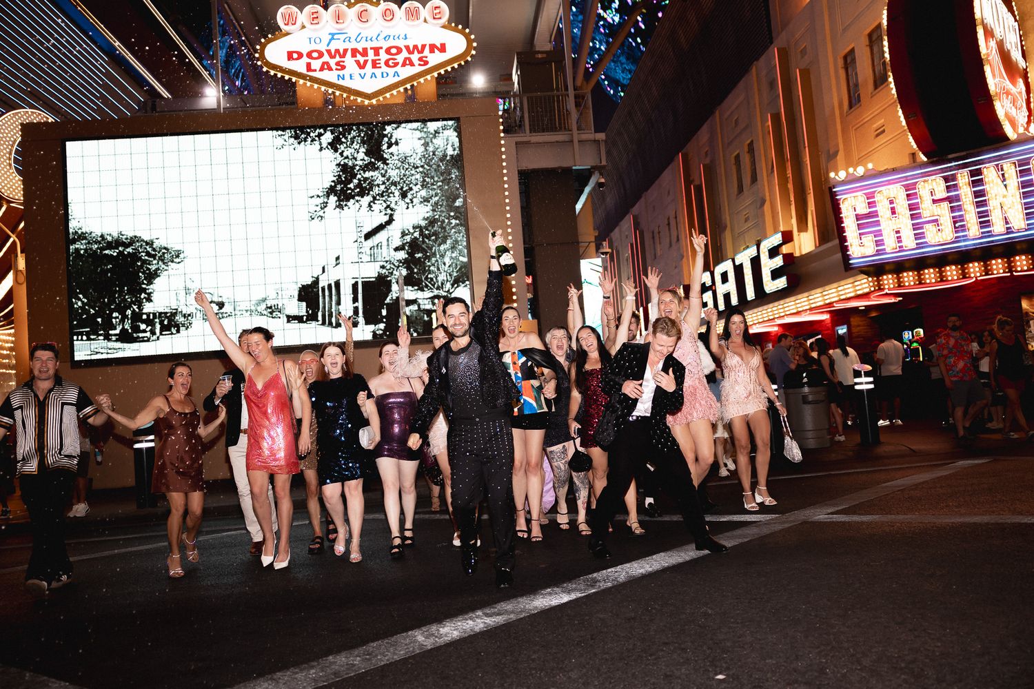 A large group of women in cocktail dresses pose on Fremont Street in downtown Las Vegas at night.