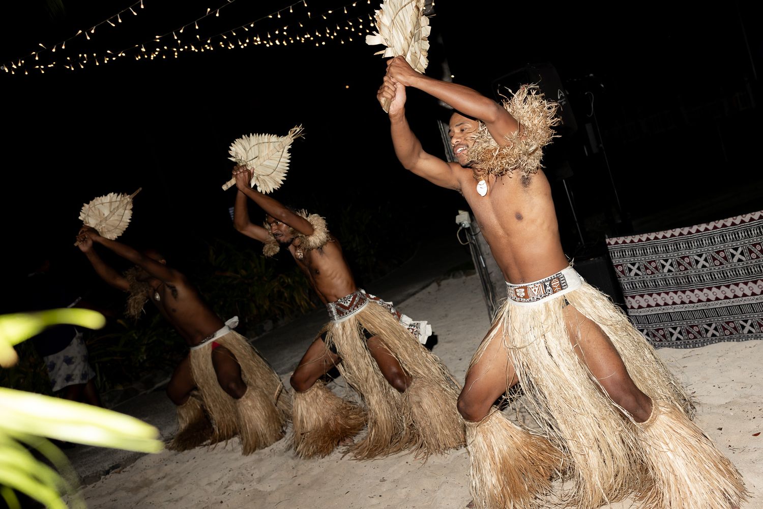 Traditional Fijian dancers in grass skirts perform cultural dance on beach at night.