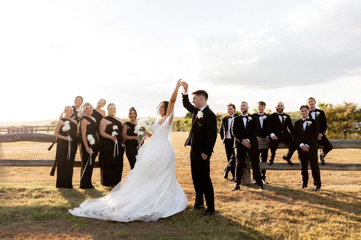 Bride and groom dance while wedding party celebrates outdoors on a sunny day at a rustic farm venue.