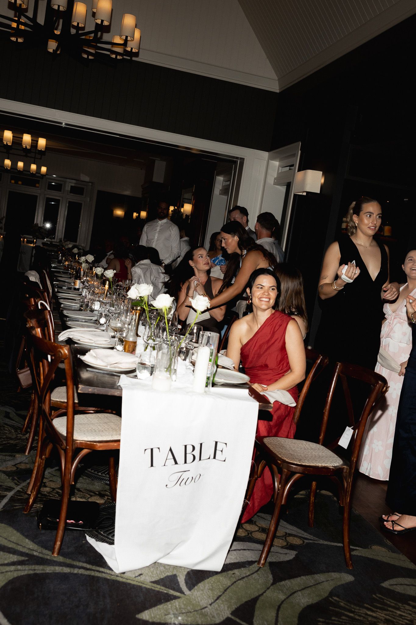 Wedding reception guests seated at elegantly set long tables with white table runners and floral centerpieces.