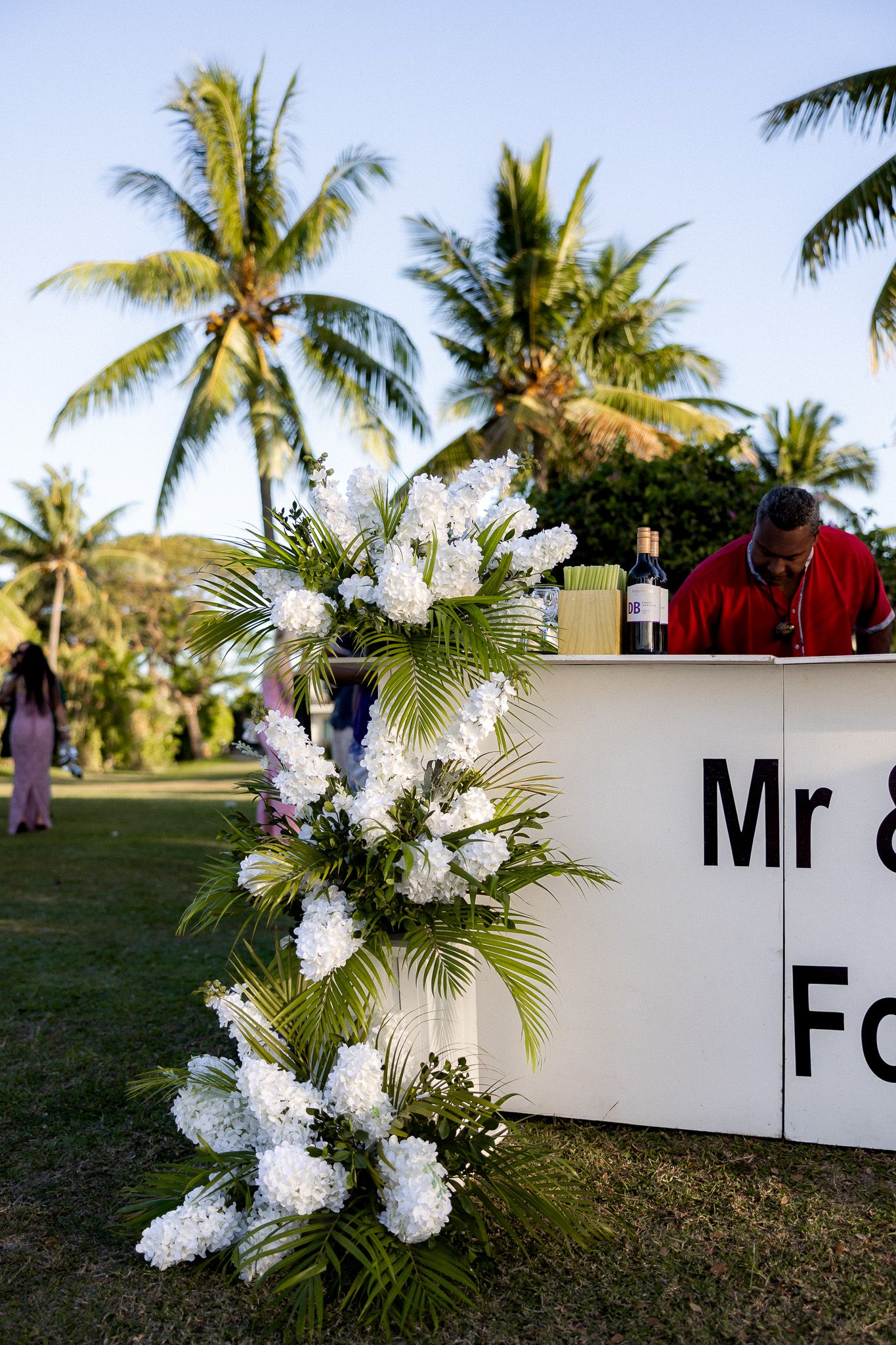 White bar decorated with tropical white floral arrangement reading Mr and Mrs at outdoor wedding.