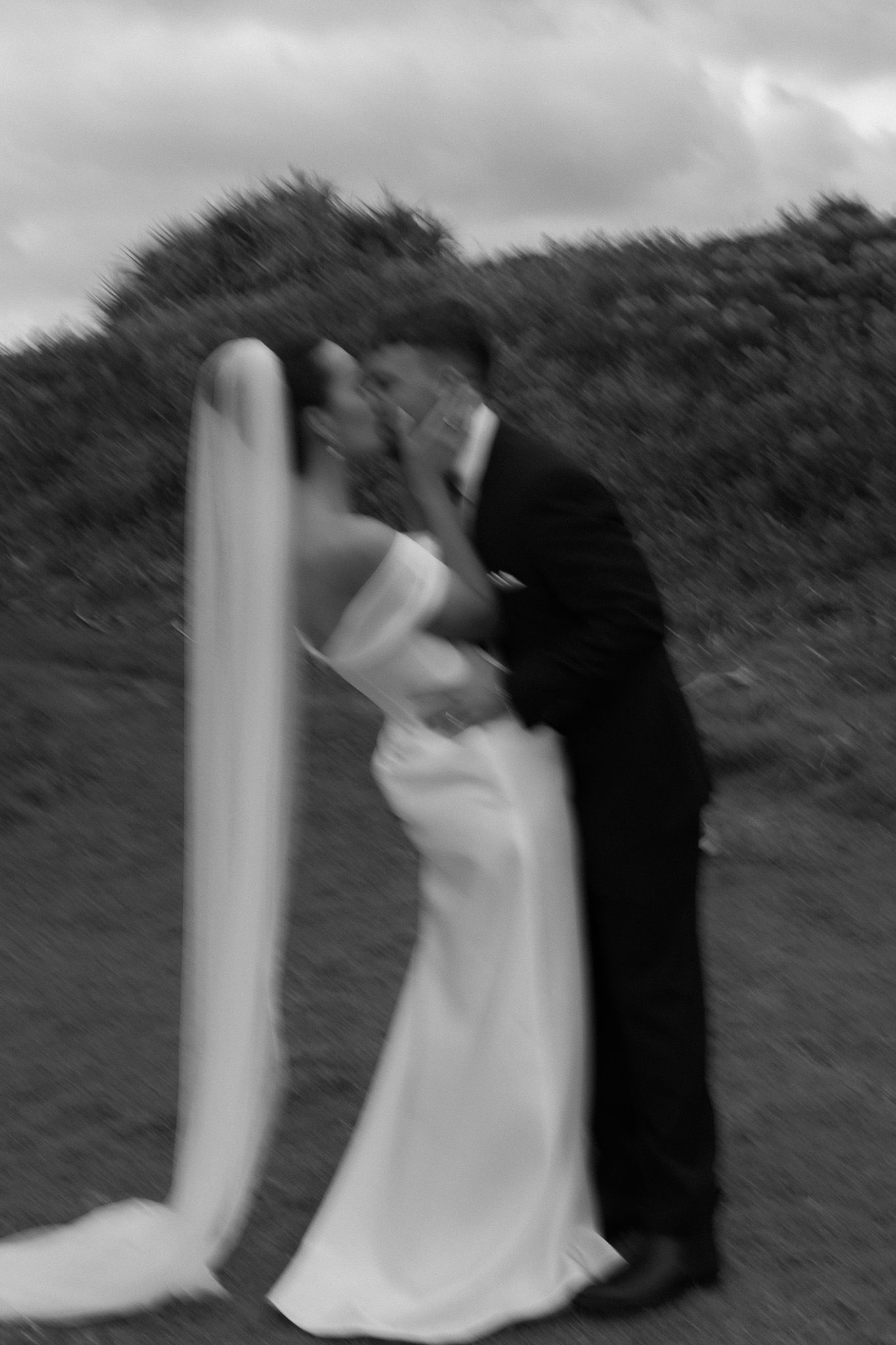 Black and white blurred photo of a bride and groom sharing a kiss outdoors on their wedding day.