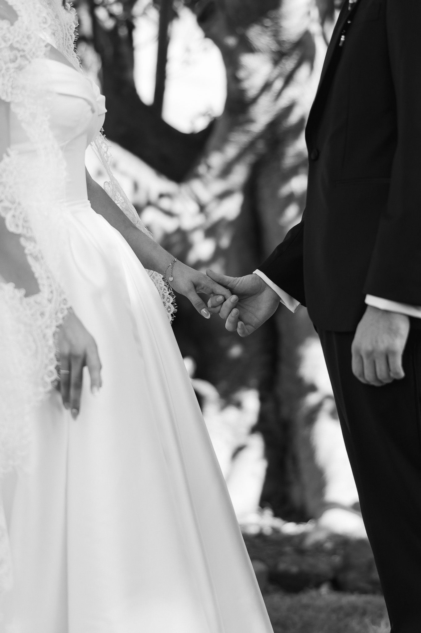 Black and white photo of a bride and groom holding hands during their outdoor wedding ceremony.