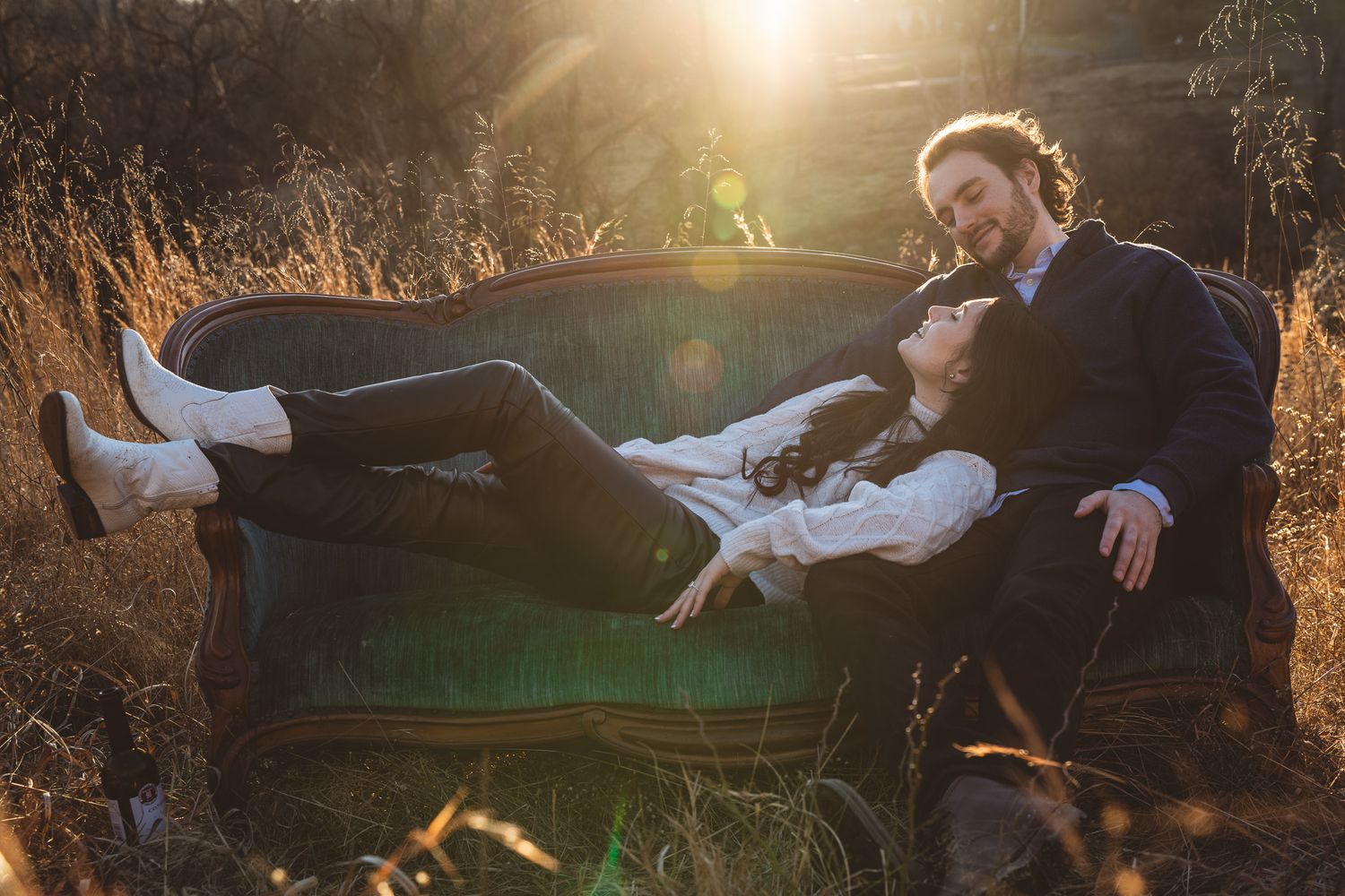 A couple relaxes on a vintage sofa in a golden field bathed in warm sunset light.
