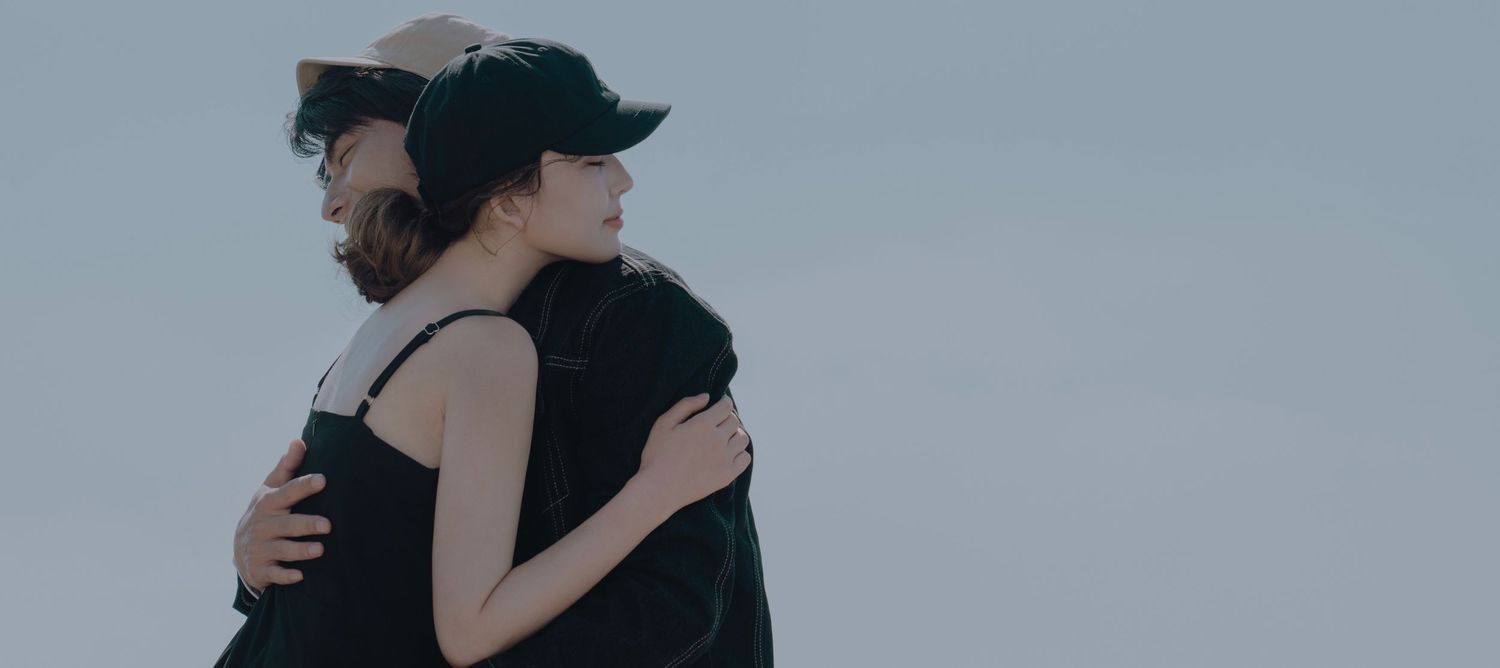 Couple embracing in a tender hug against a soft gray sky outdoors.
