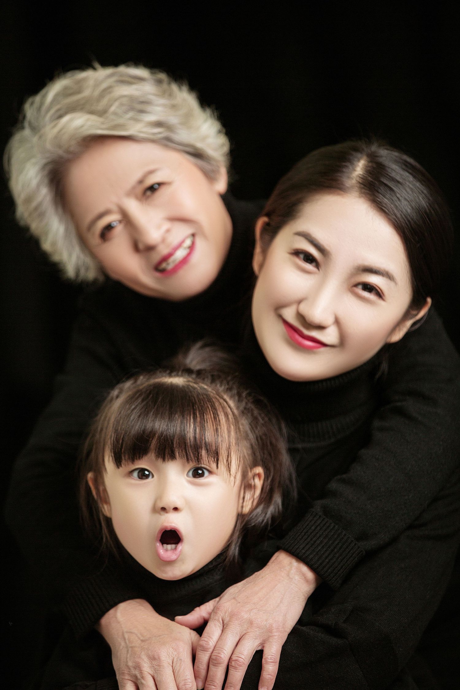 Three generations of Asian women smile together, with grandmother, mother, and surprised toddler posing.