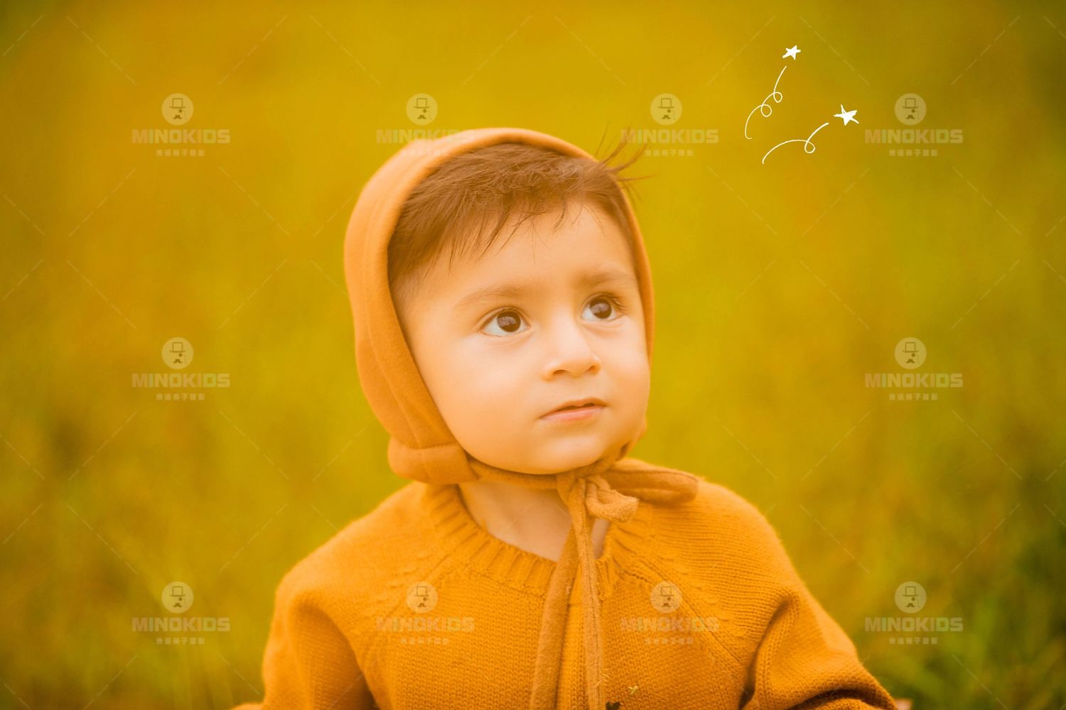 Adorable baby in mustard knit hooded jacket gazes upward against warm golden yellow background.