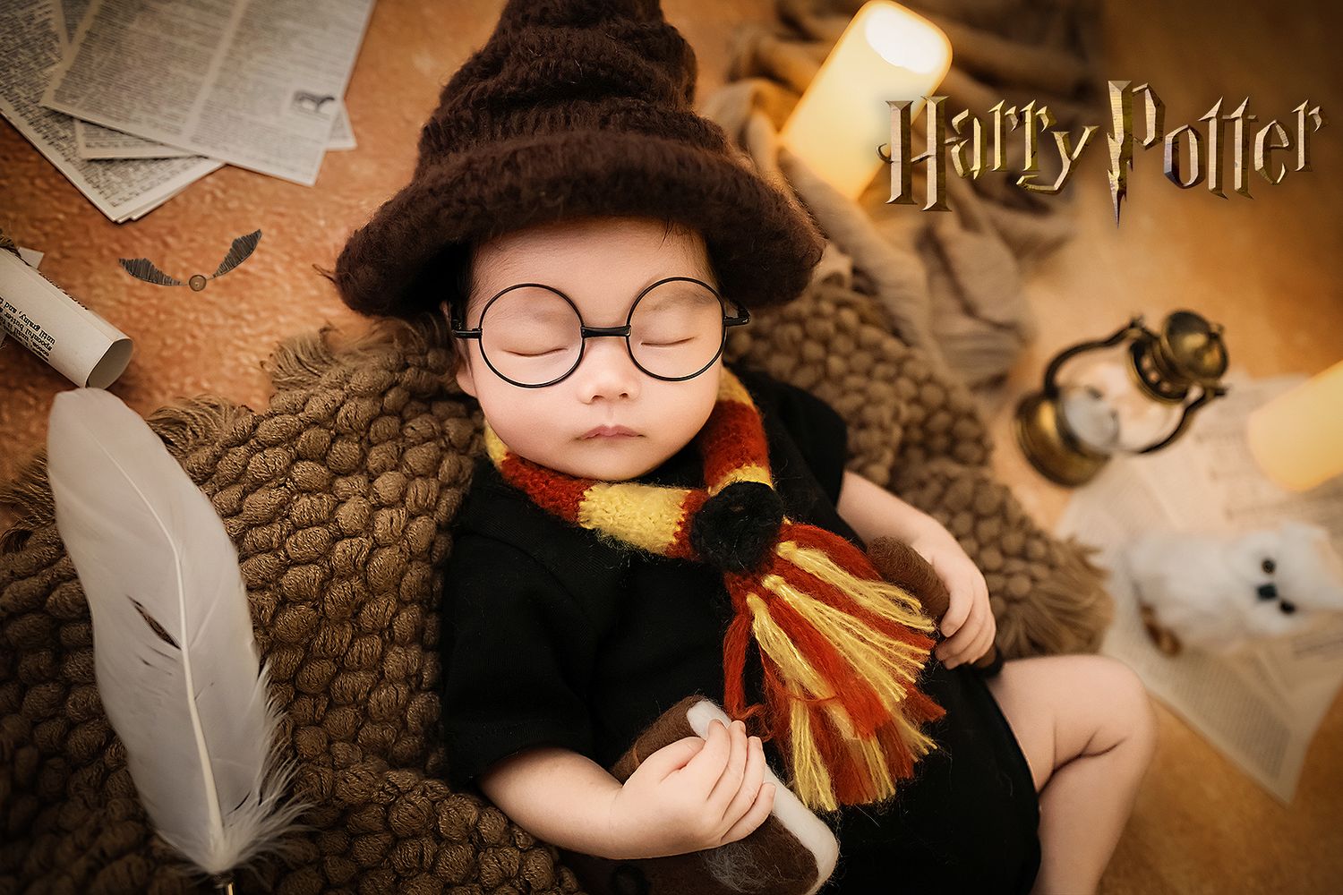 Sleeping newborn baby dressed as Harry Potter holding wand wearing sorting hat and round glasses.
