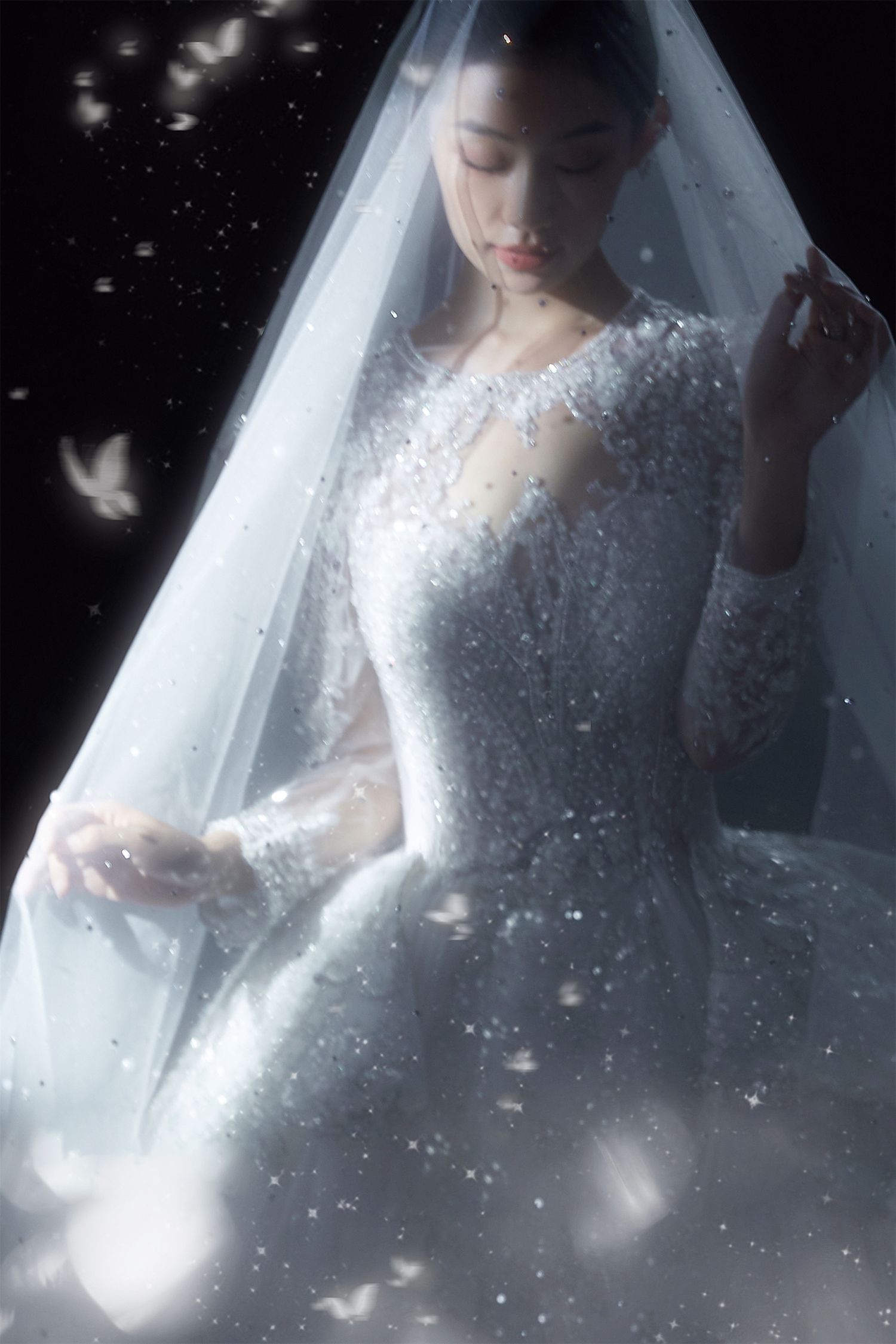 Bride in stunning beaded white wedding dress reaching out under veil with floating butterflies.