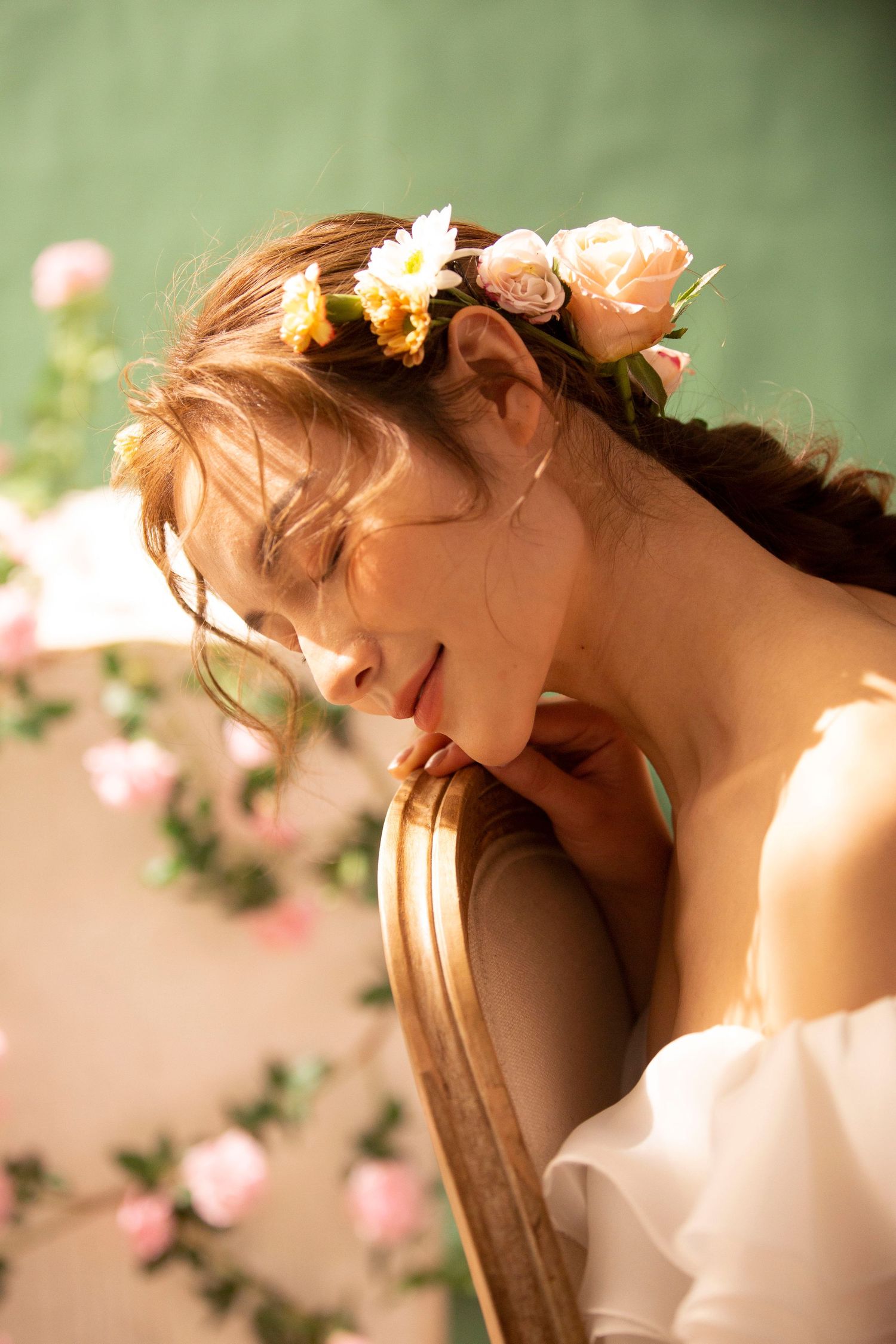 A bride wearing a floral crown rests her chin on a golden picture frame surrounded by roses.