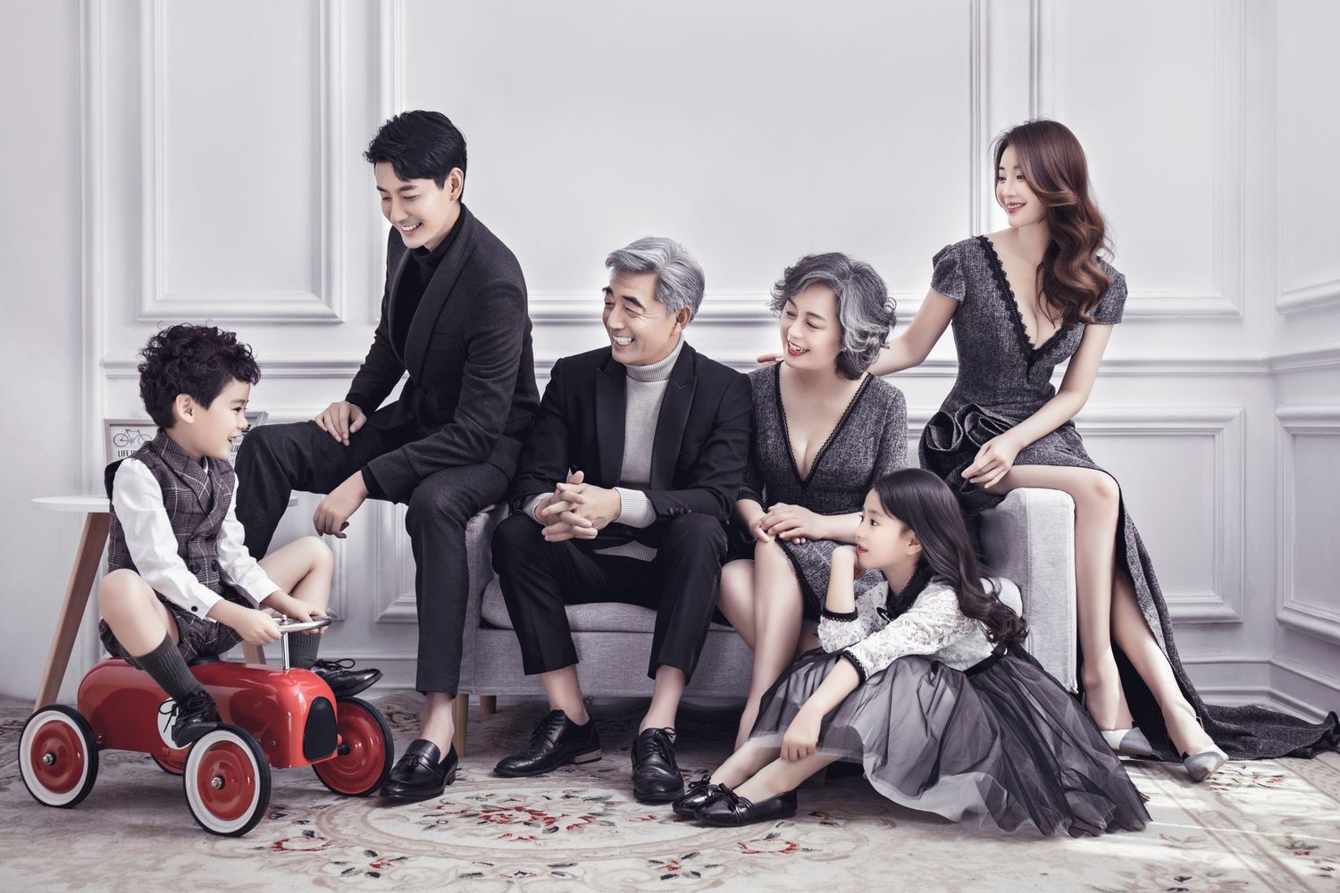 Multigenerational Asian family in casual elegant attire sharing a relaxed moment together on a studio sofa.
