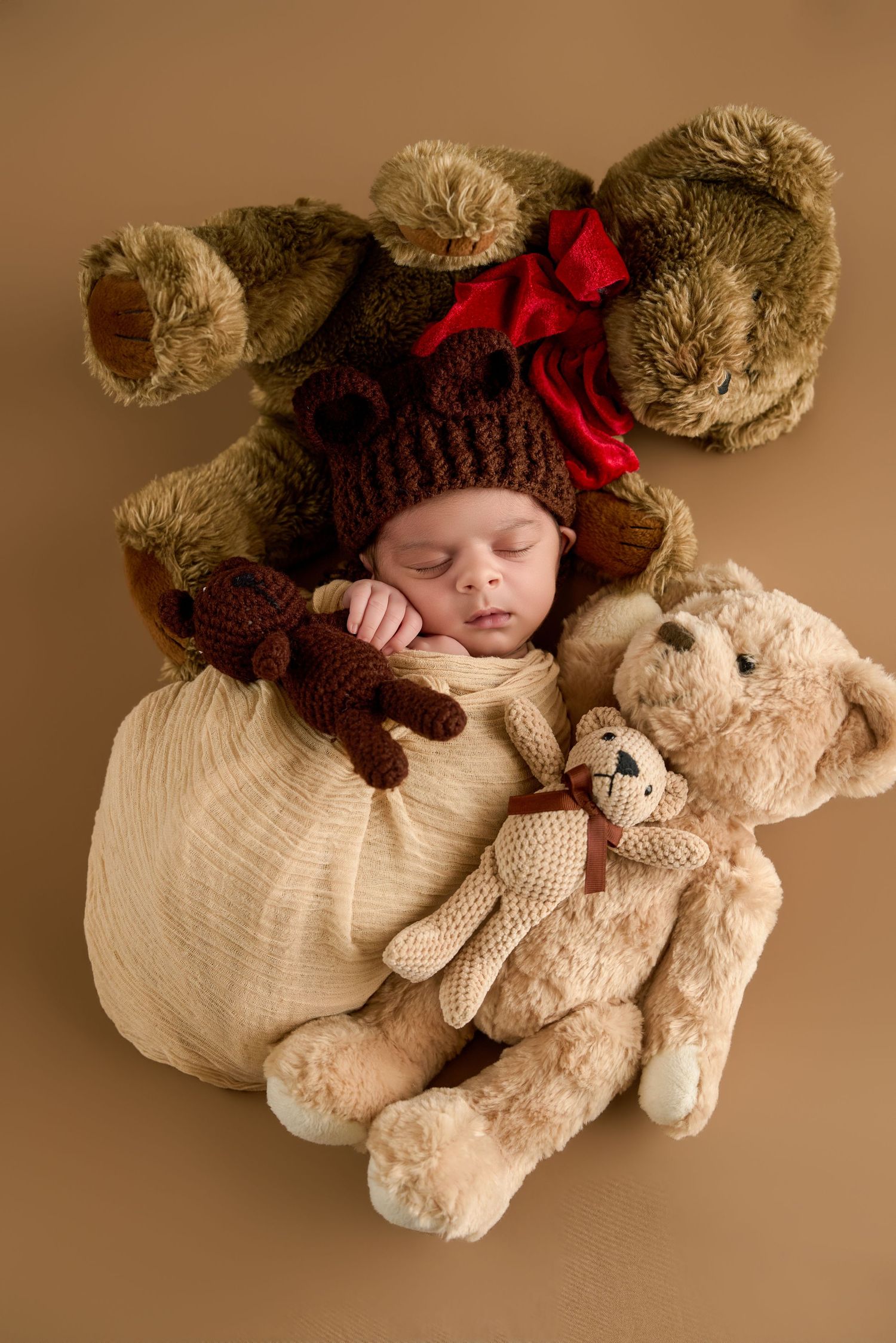 Sleeping newborn baby in bear hat surrounded by teddy bears on brown background.