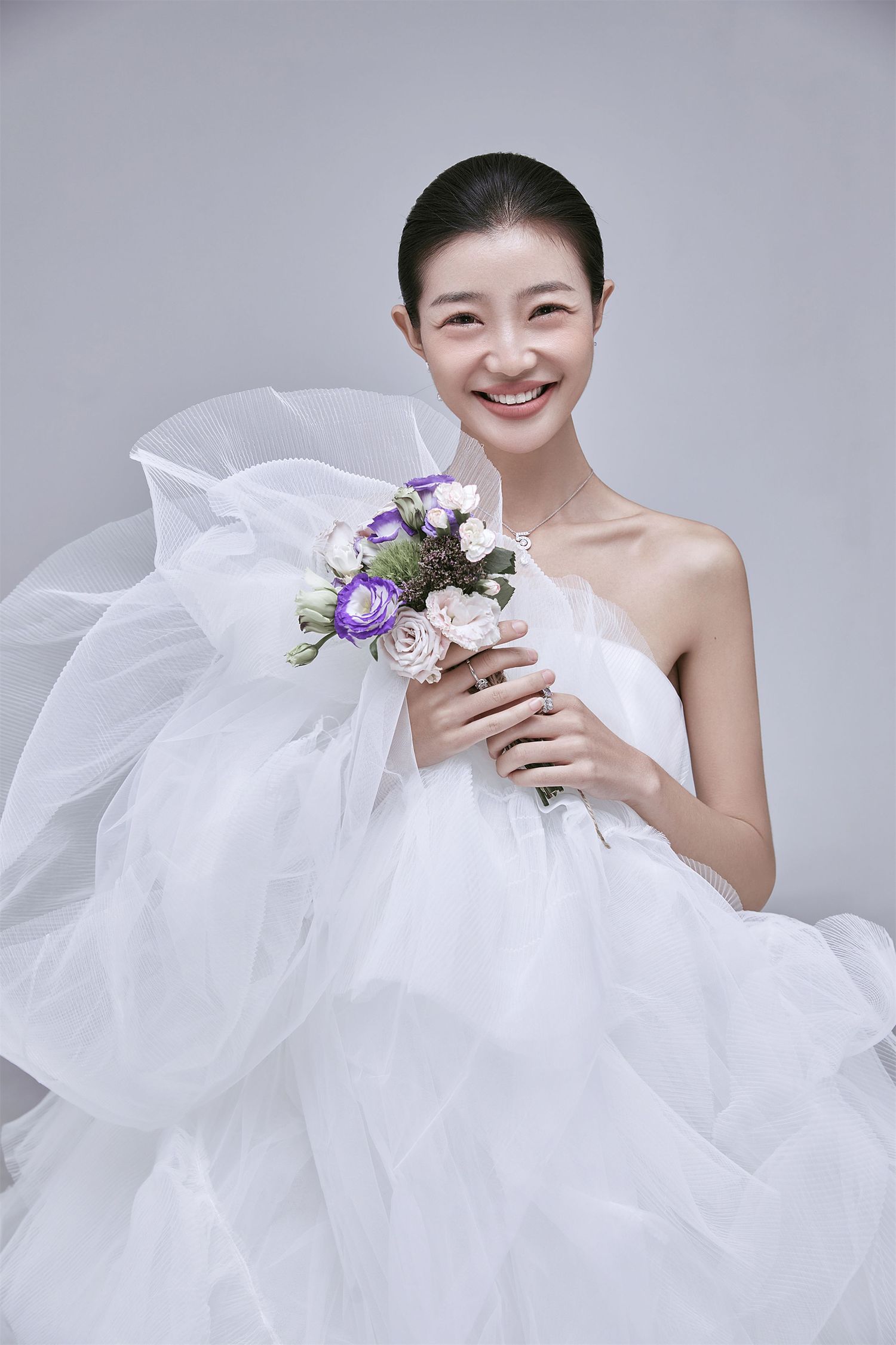A joyful bride in a white strapless tulle gown holds a bouquet of purple and white roses.