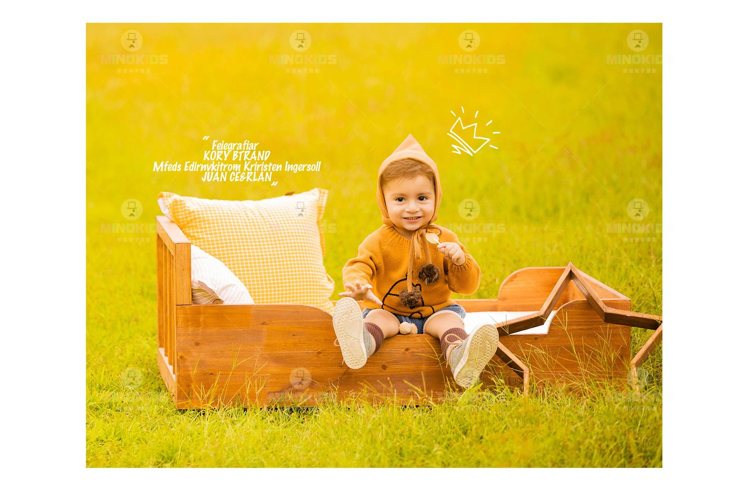 Happy toddler in yellow outfit sits on wooden bed prop in sunny green meadow outdoor photoshoot.