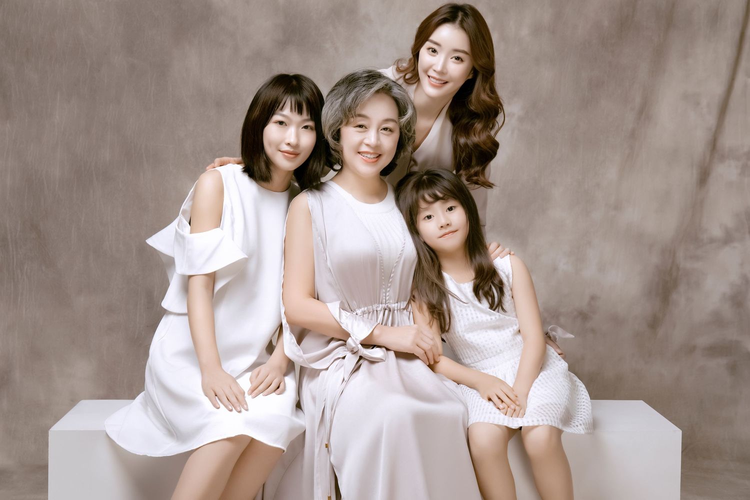 Four Asian women of different ages in white outfits smiling together in a studio family portrait.
