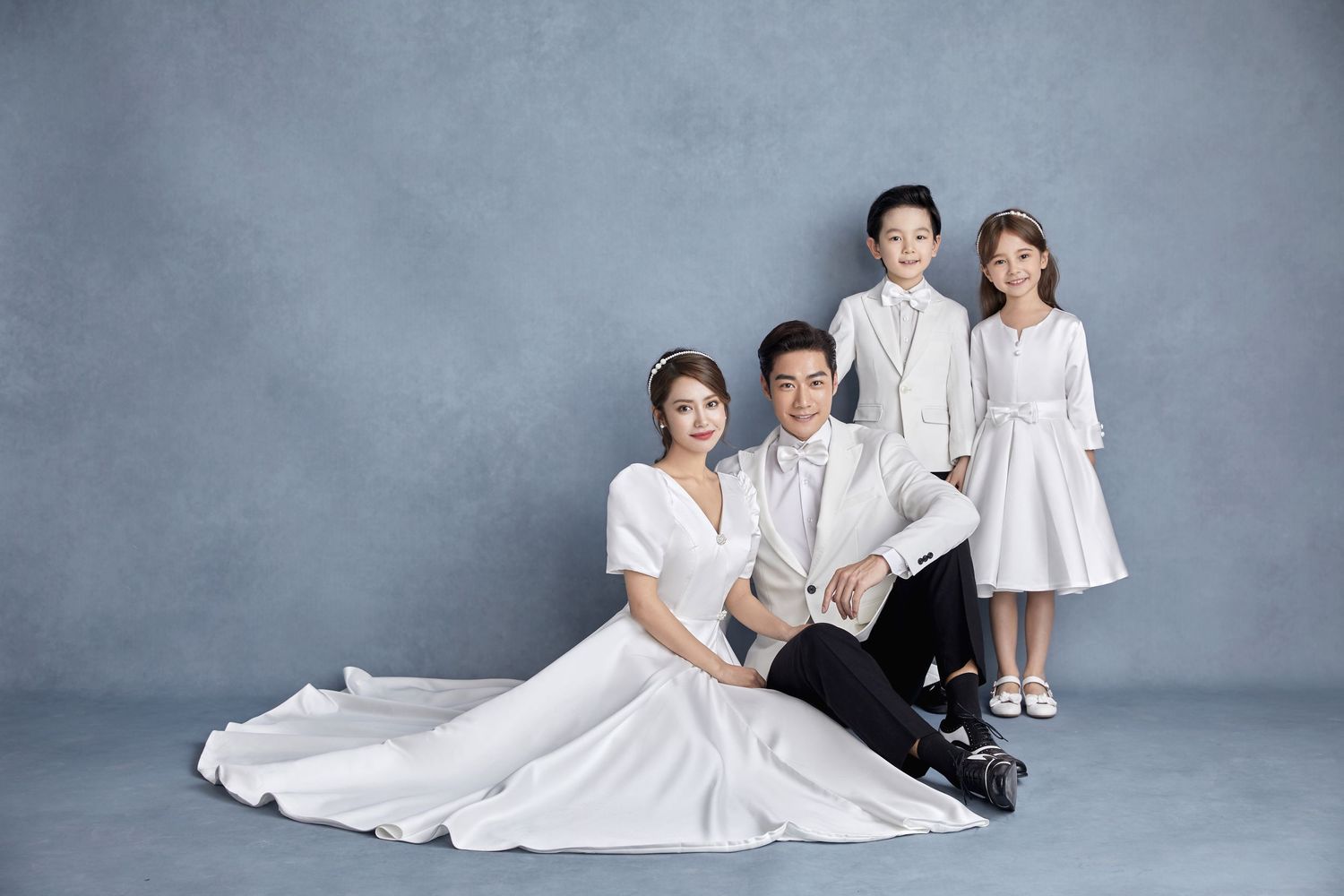 Family of four in elegant white outfits posing for a formal studio wedding anniversary portrait.