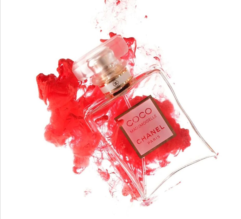 Chanel Coco Mademoiselle perfume bottle surrounded by dramatic red ink splash on white background.