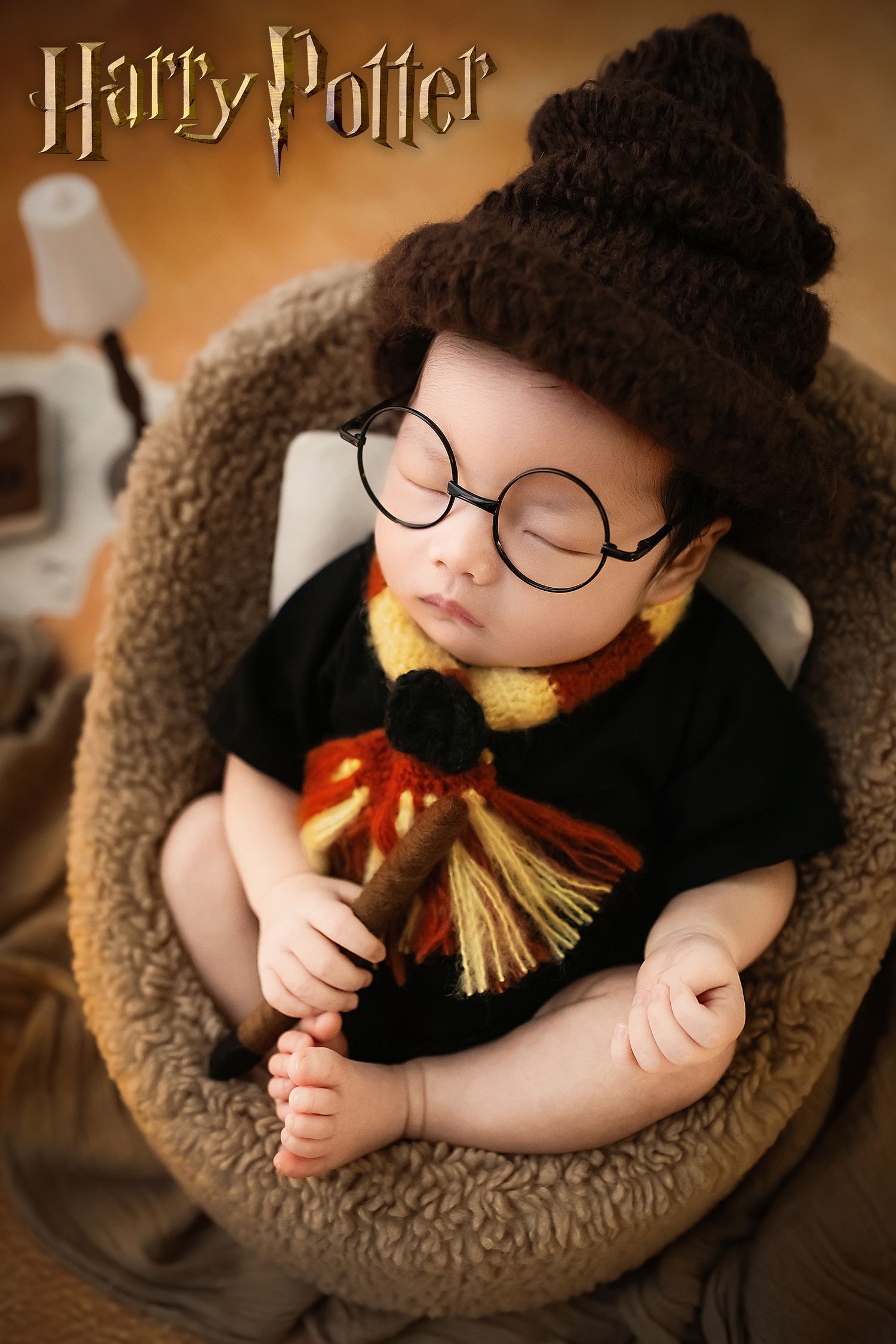 Close-up of sleeping newborn dressed as Harry Potter with sorting hat, glasses, and Gryffindor scarf.