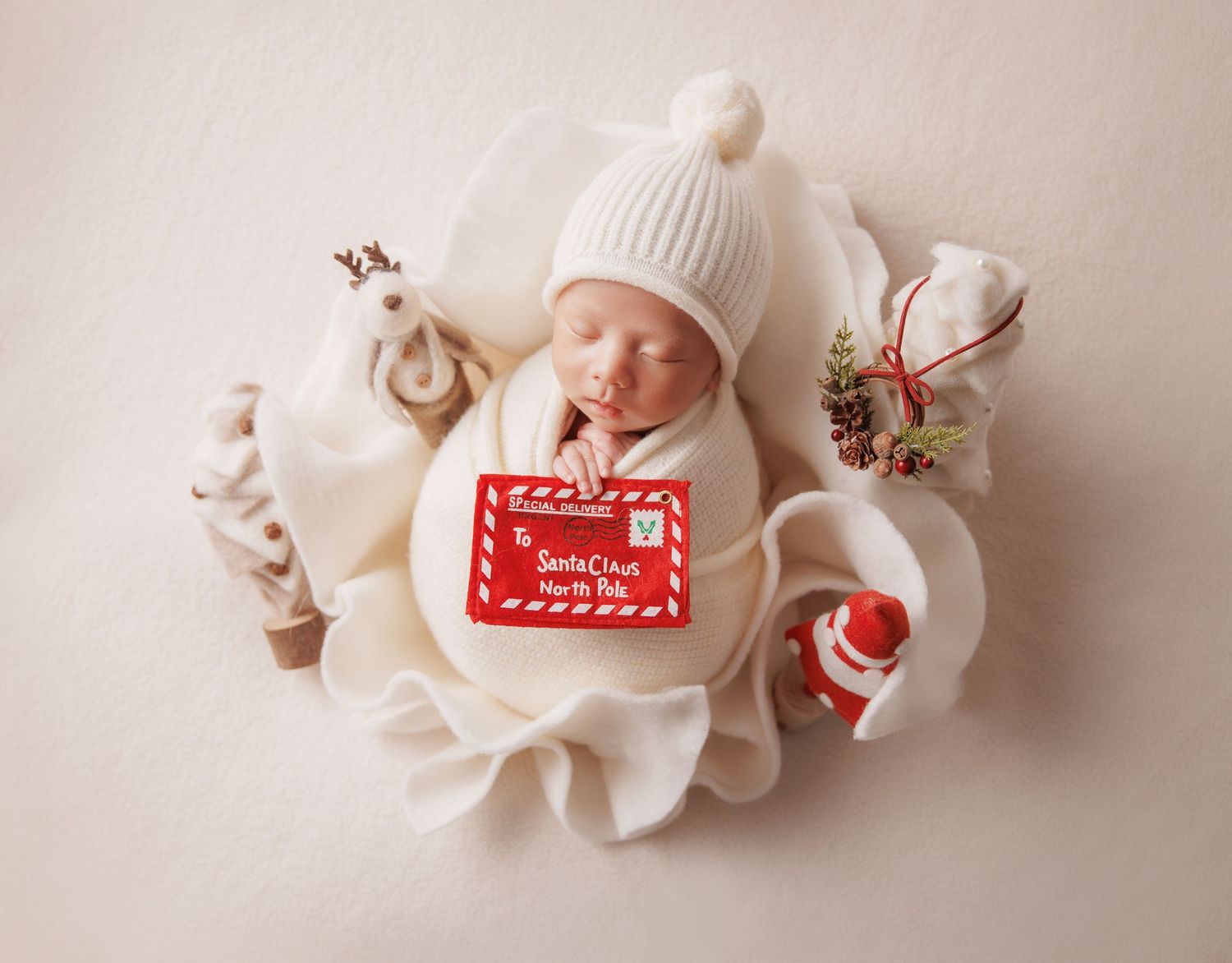Swaddled newborn in white knit hat rests in ruffled basket with Santa letter and Christmas decorations.