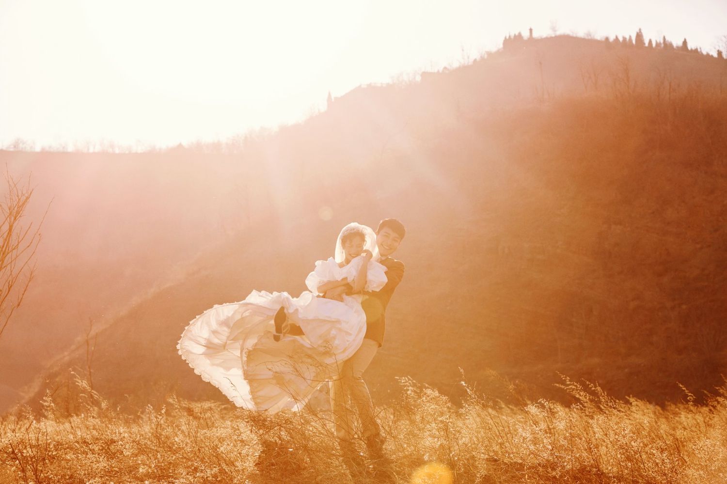 Groom lifting bride in golden sunlight with mountain backdrop.