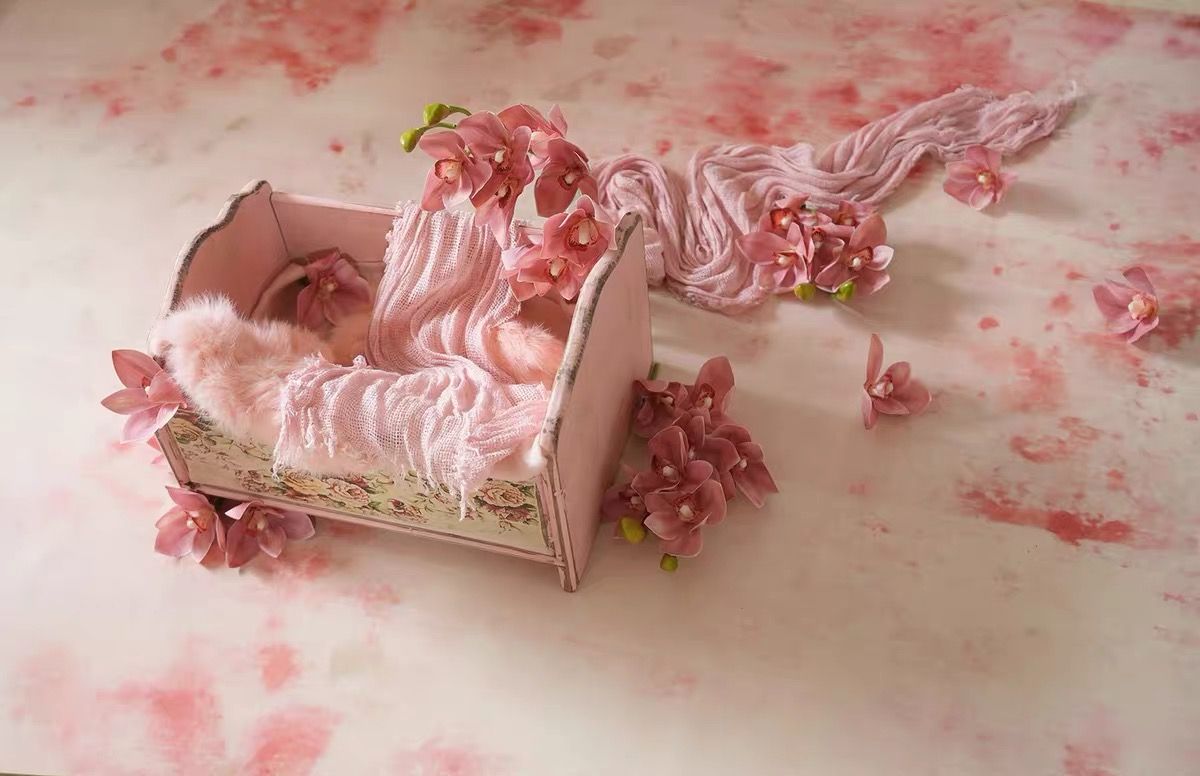 Newborn baby sleeping in a pink miniature wooden bed with floral decorations for a dreamy photo shoot.