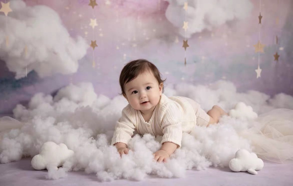 Baby crawling on fluffy white clouds with stars on a purple backdrop in a dreamy photo shoot.