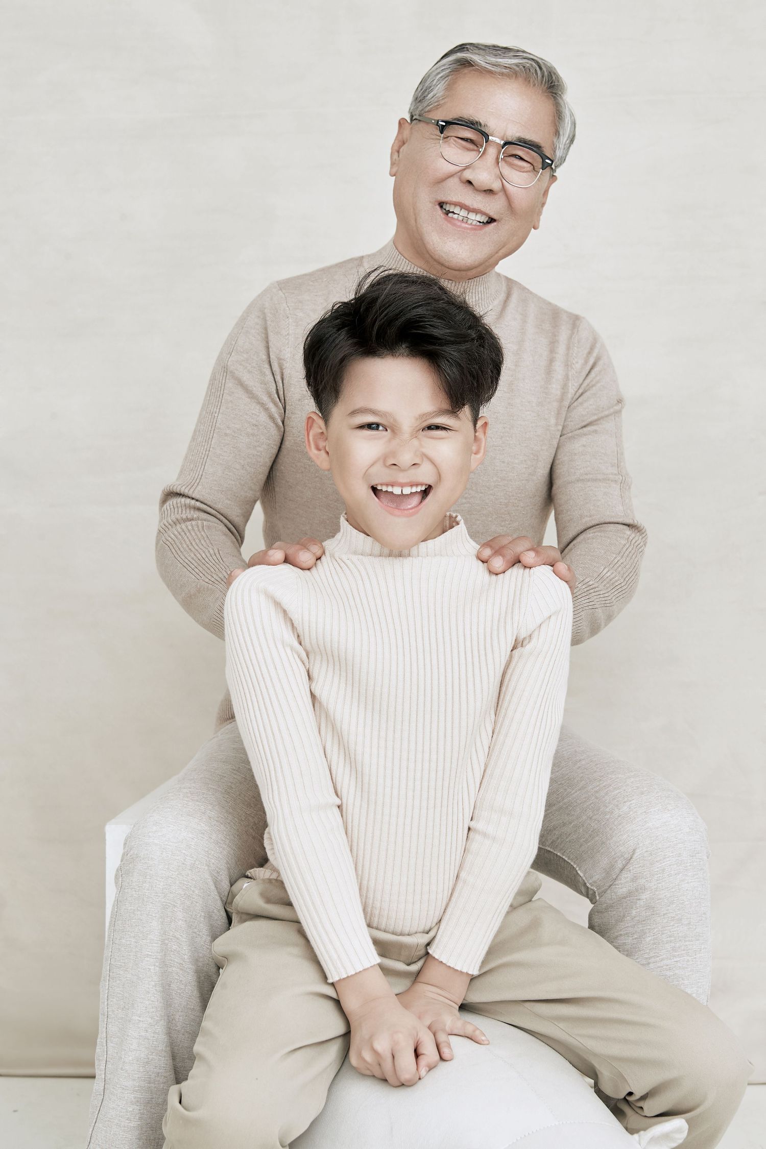 A cheerful Asian boy laughing while an older man with glasses places hands on his shoulders in a studio.