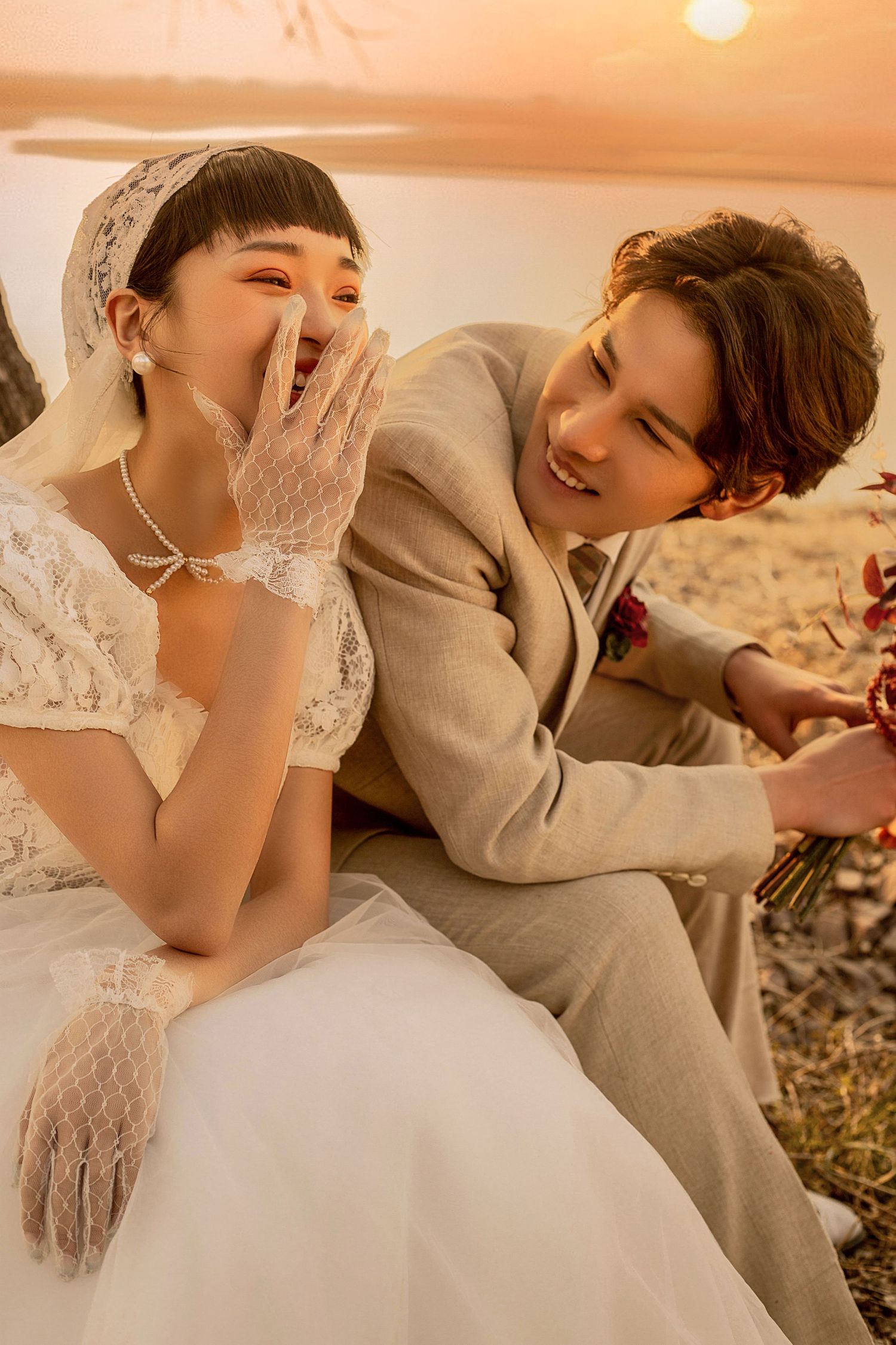 Joyful Asian bride and groom laugh together outdoors during warm sunset wedding photography session.