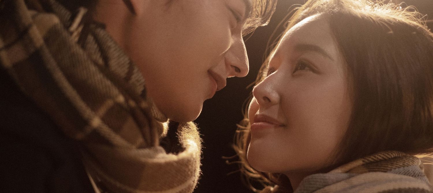 Close-up of a romantic couple almost kissing in warm golden sunlight wearing cozy scarves.