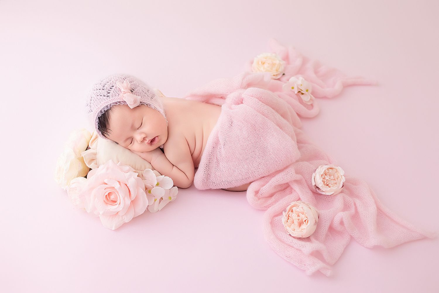 Newborn baby girl sleeping on pink knit blanket with pink roses and lavender crown headband.