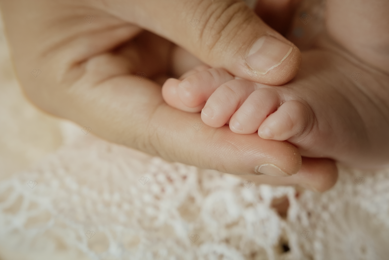 Close-up of a newborn baby's tiny fingers gently grasping an adult's hand on a white lace blanket.