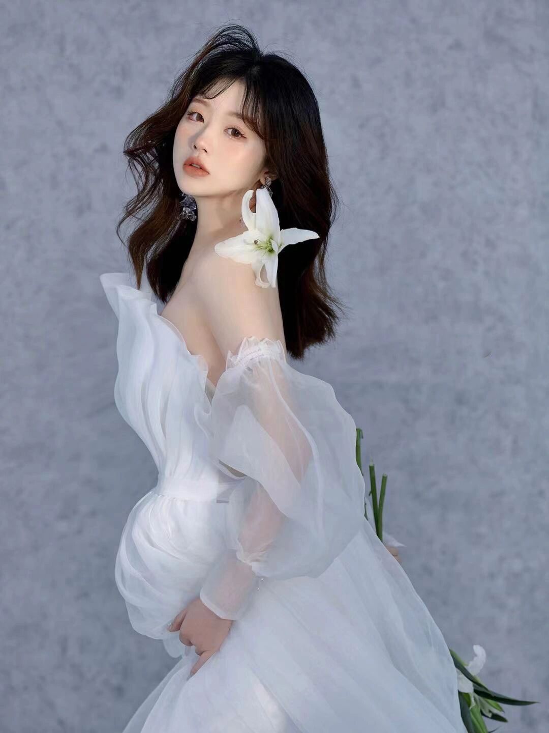 Young woman in white off-shoulder tulle gown holding white lily flowers in elegant portrait photography.