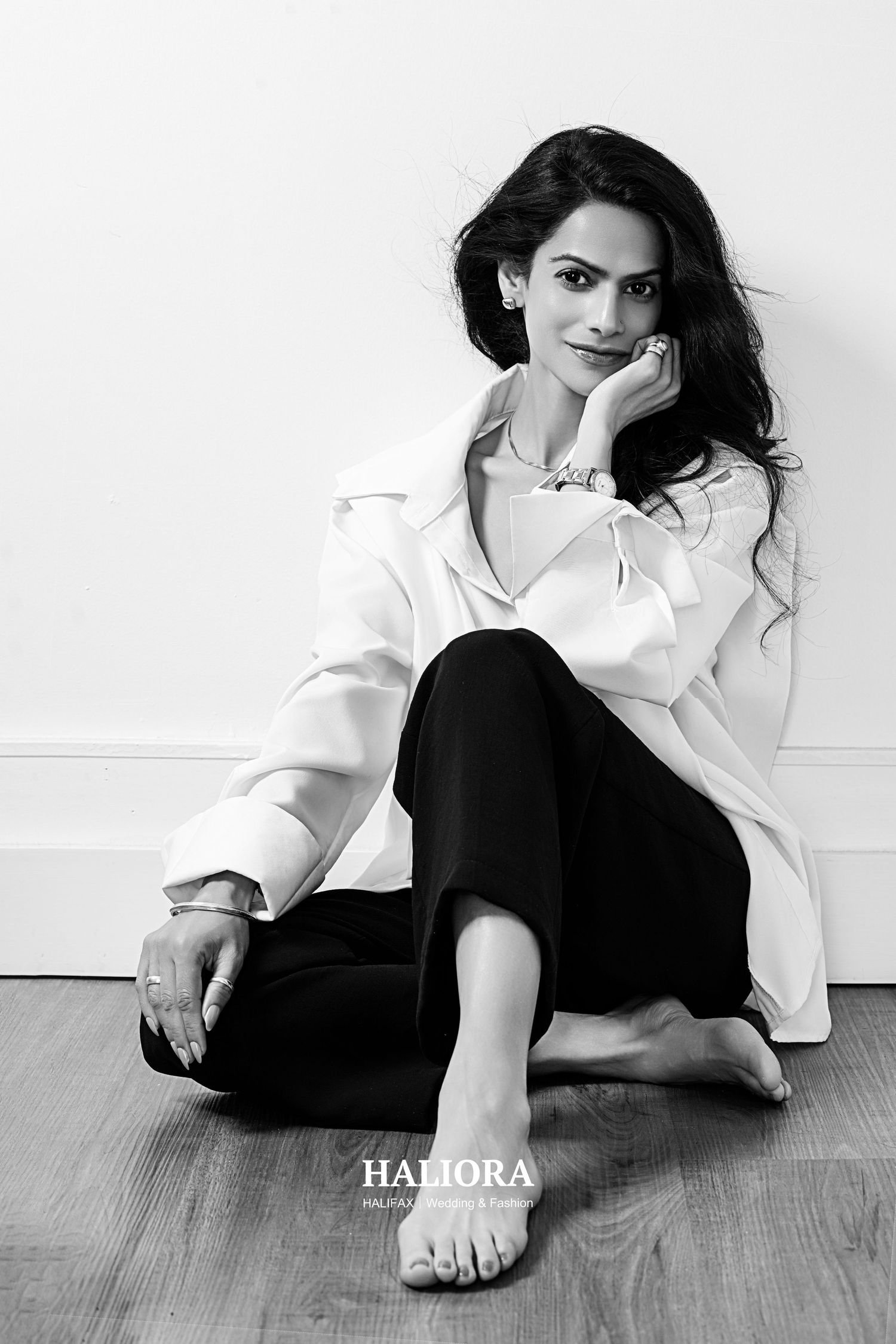 Black and white portrait of elegant woman in white shirt and black pants sitting on wooden floor, relaxed pose.